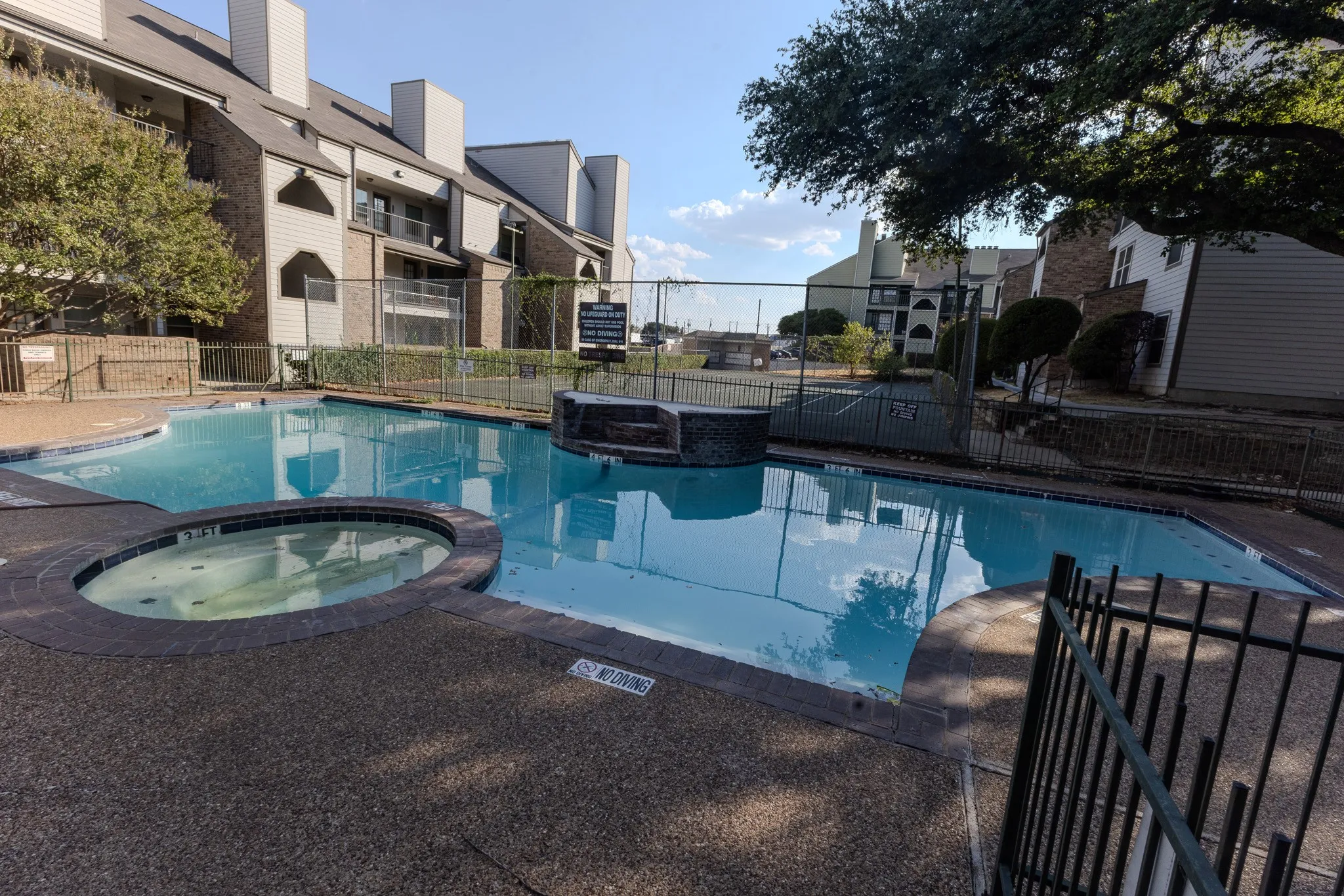 Outdoor pool with an integrated spa, surrounded by a chain-link fence