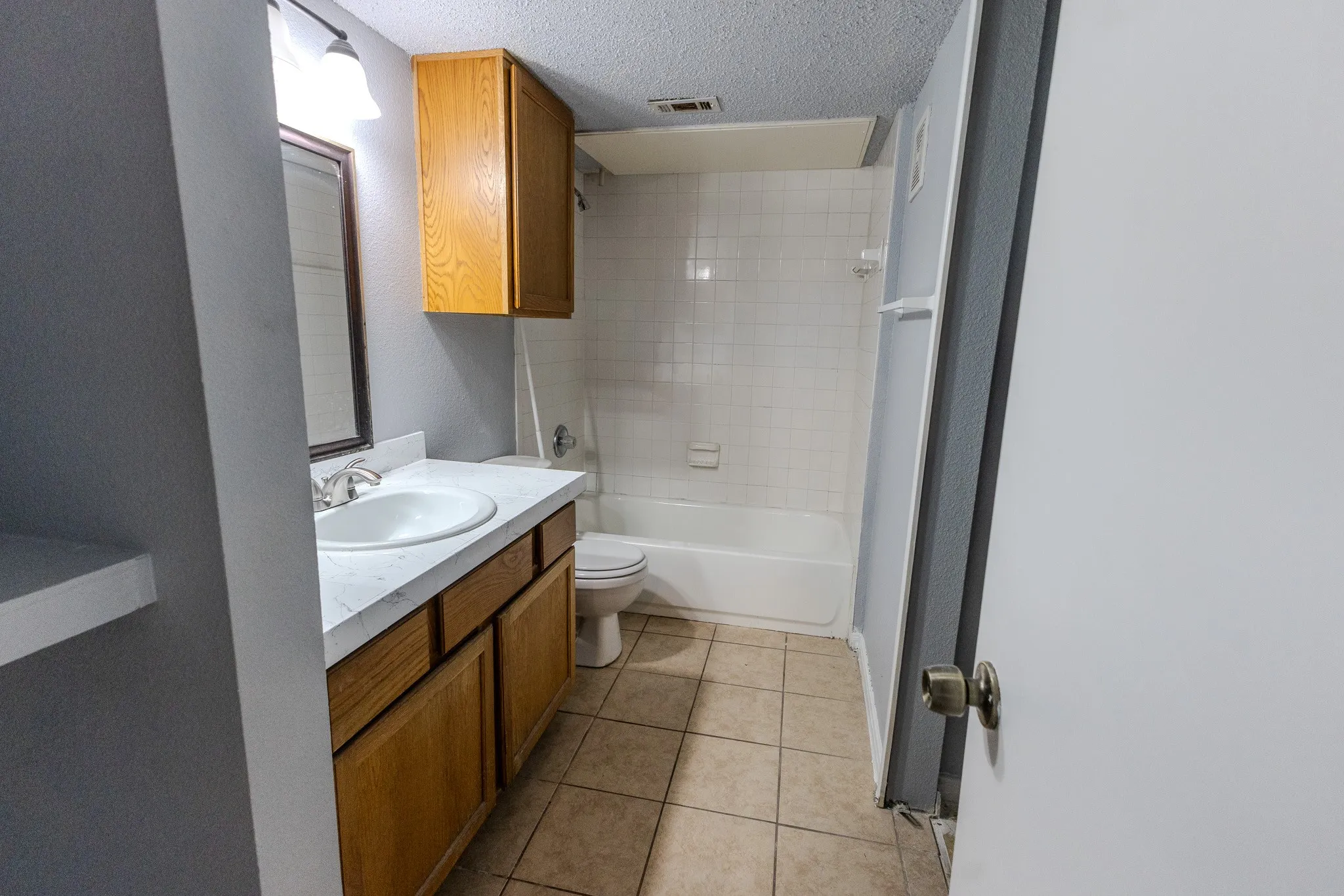 Bathroom featuring a vanity with wood-finish cabinetry, a white countertop with an integrated sink, a mirrored medicine cabinet, a full-size bathtub, and tiled flooring