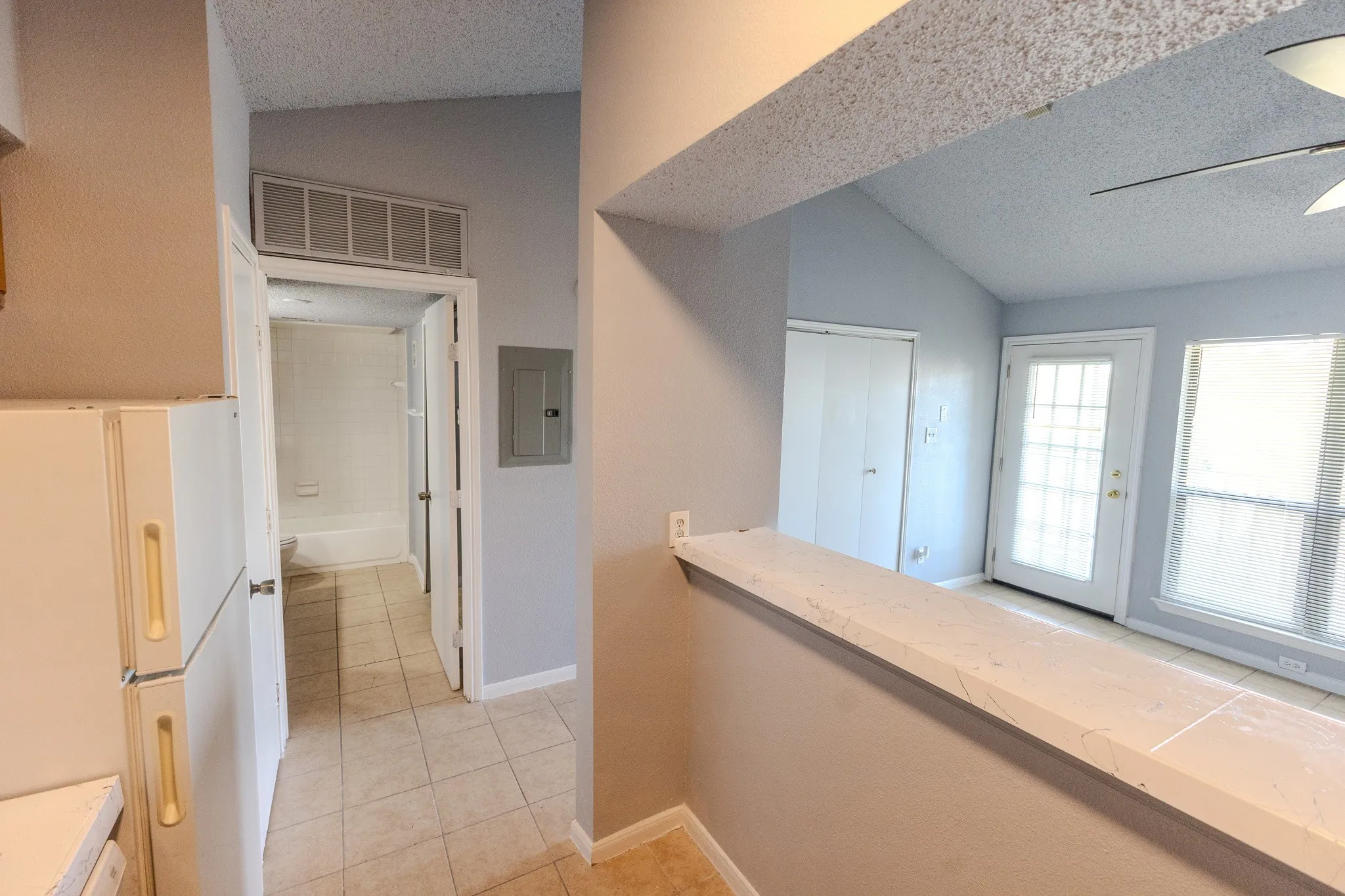 Kitchen pass-through with a light-colored countertop, vaulted ceiling, and tiled flooring