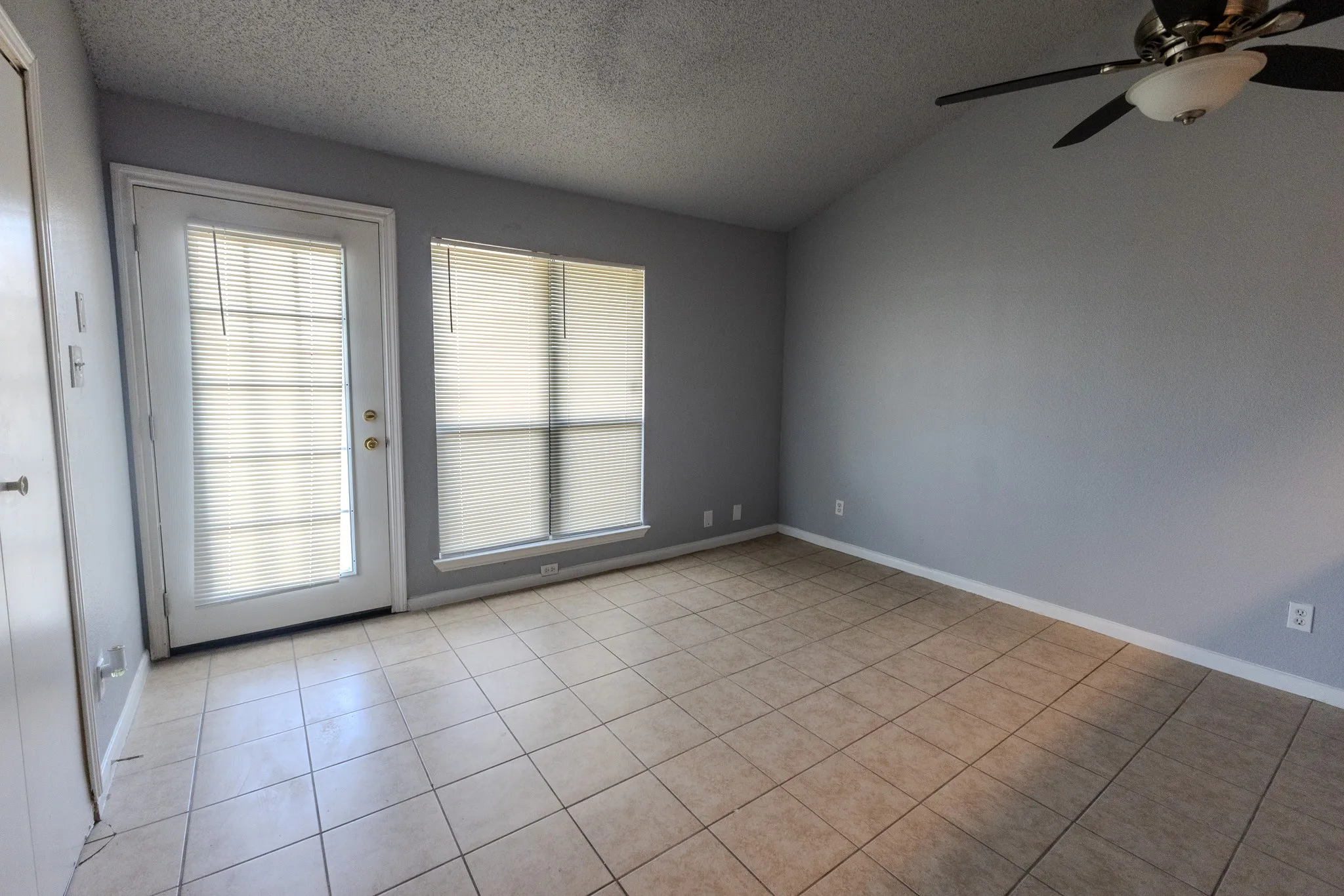 Tile flooring, vaulted ceiling, ceiling fan with integrated lighting, glass-paneled door, and a large window