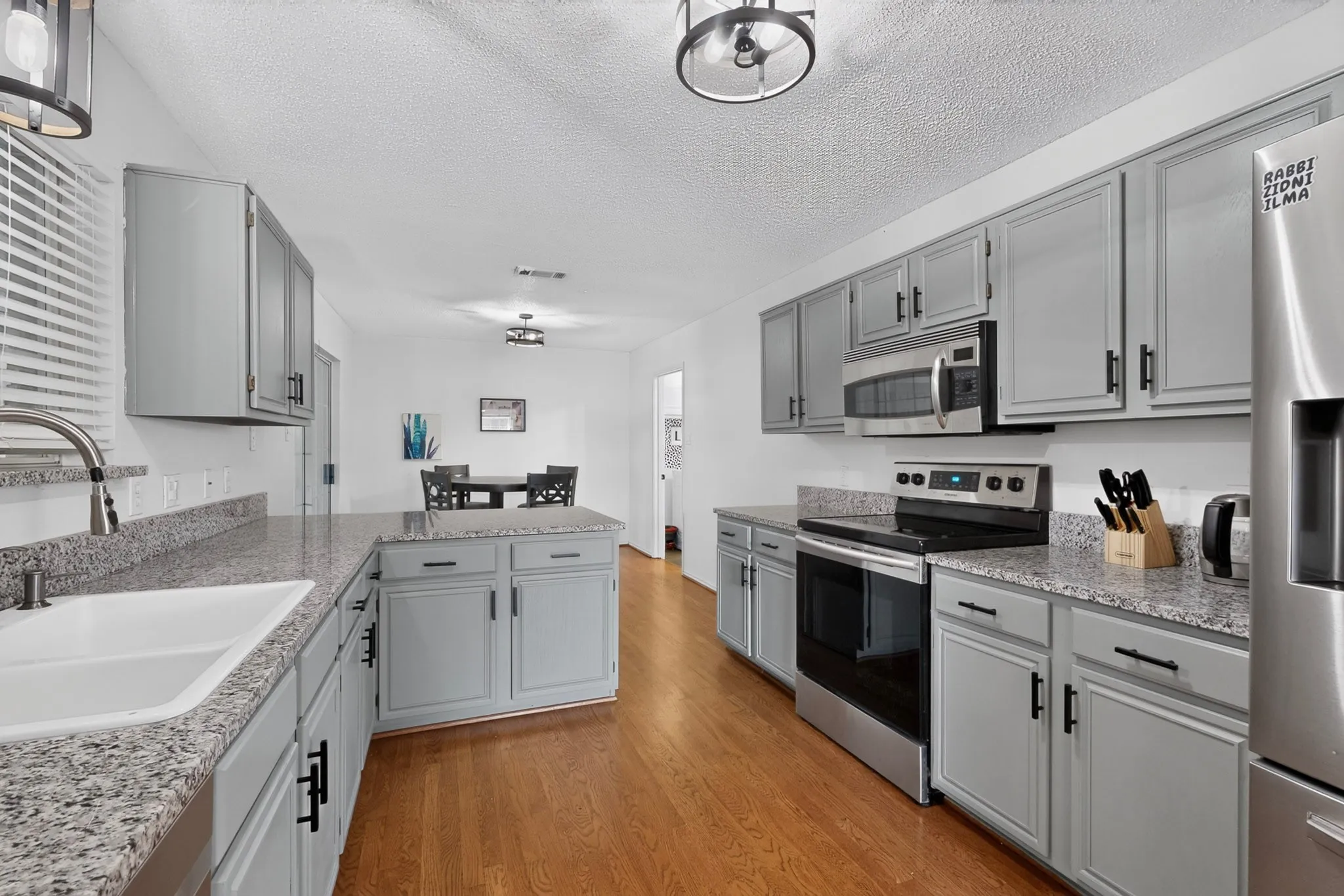 Wood-finish flooring, gray cabinetry with black hardware, white double basin sink, stainless steel appliances, and light-toned countertops