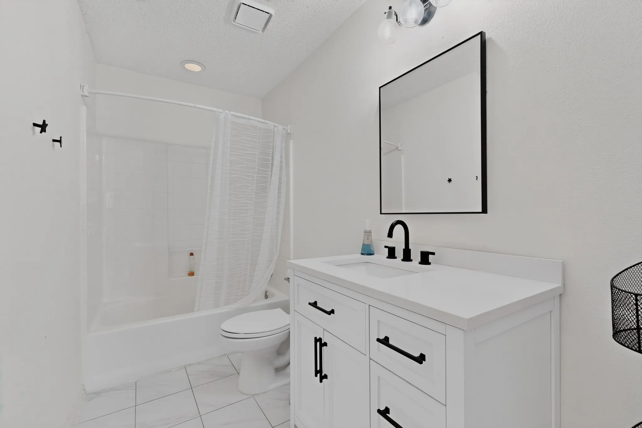 White vanity with a white countertop, black fixtures, framed mirror, and tiled flooring