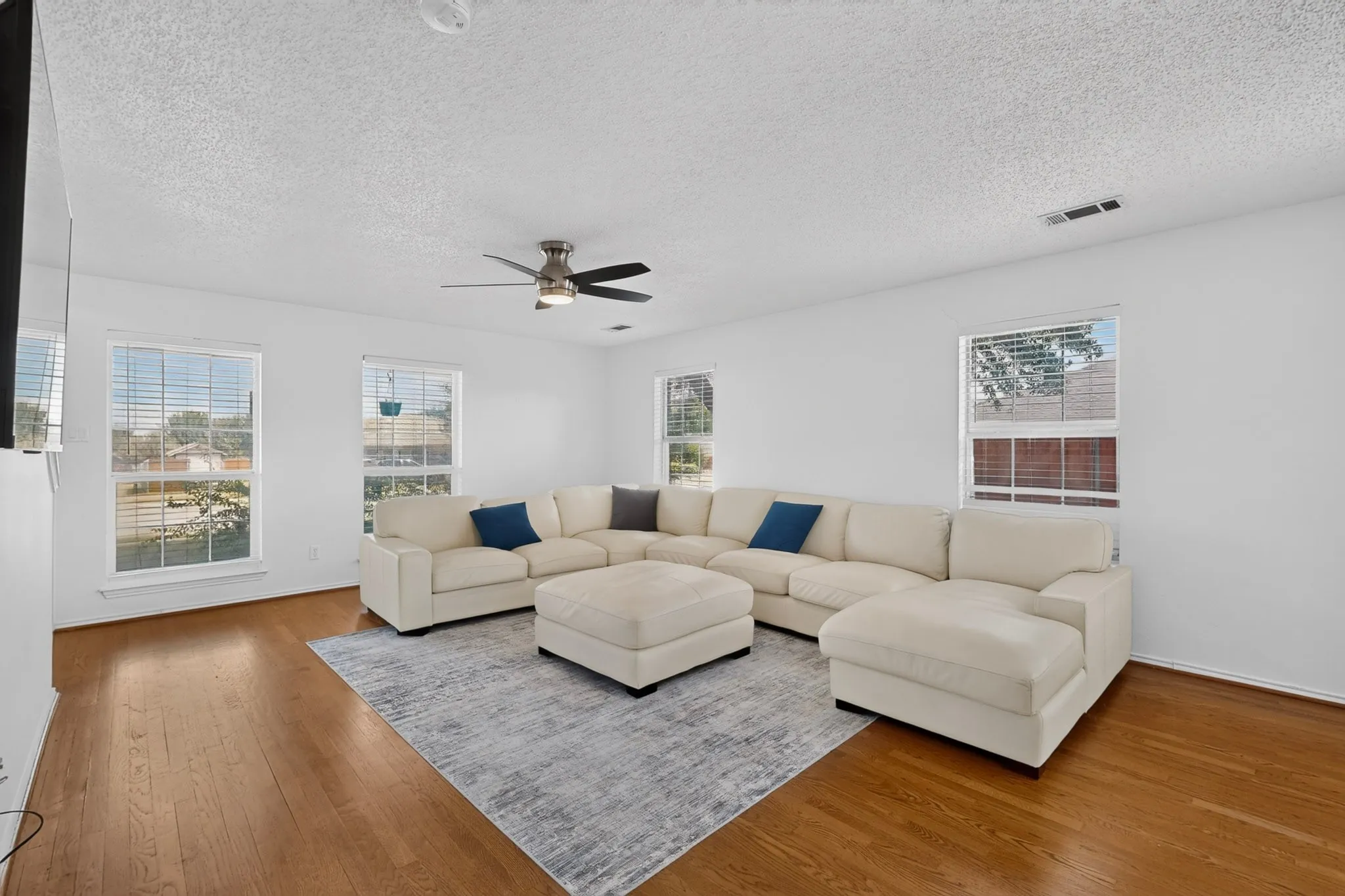Living area featuring wood-finish flooring, multiple windows, a ceiling fan with integrated lighting, and white painted walls