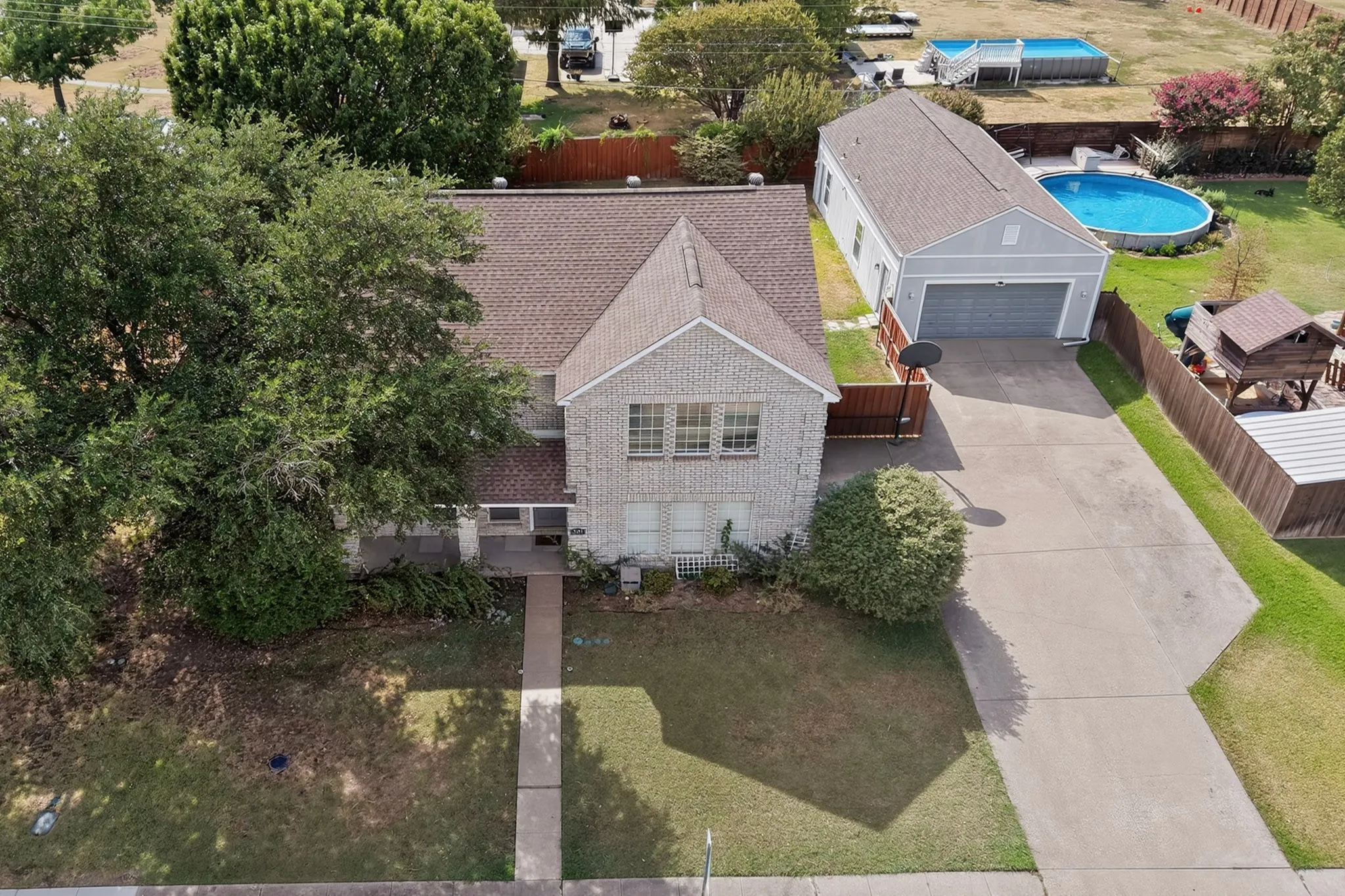Brick exterior residence featuring a detached garage, elongated driveway, and established trees