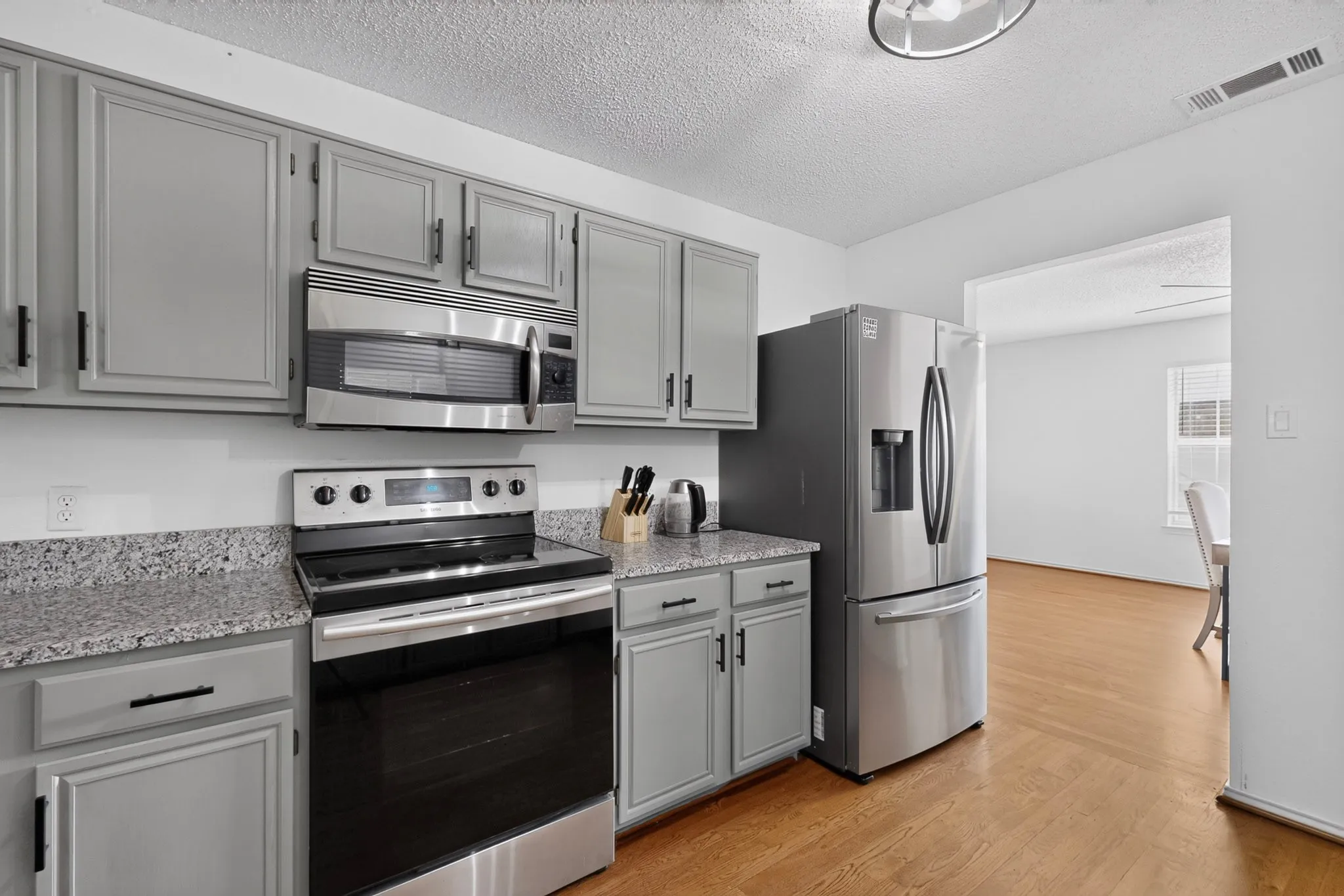 Kitchen featuring light gray cabinetry, stainless steel appliances, speckled countertops, and wood-finish flooring