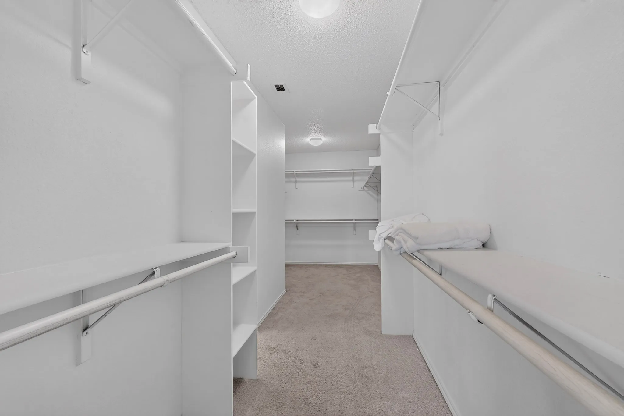 Expansive closet featuring integrated shelving, multiple hanging rods, and carpet flooring
