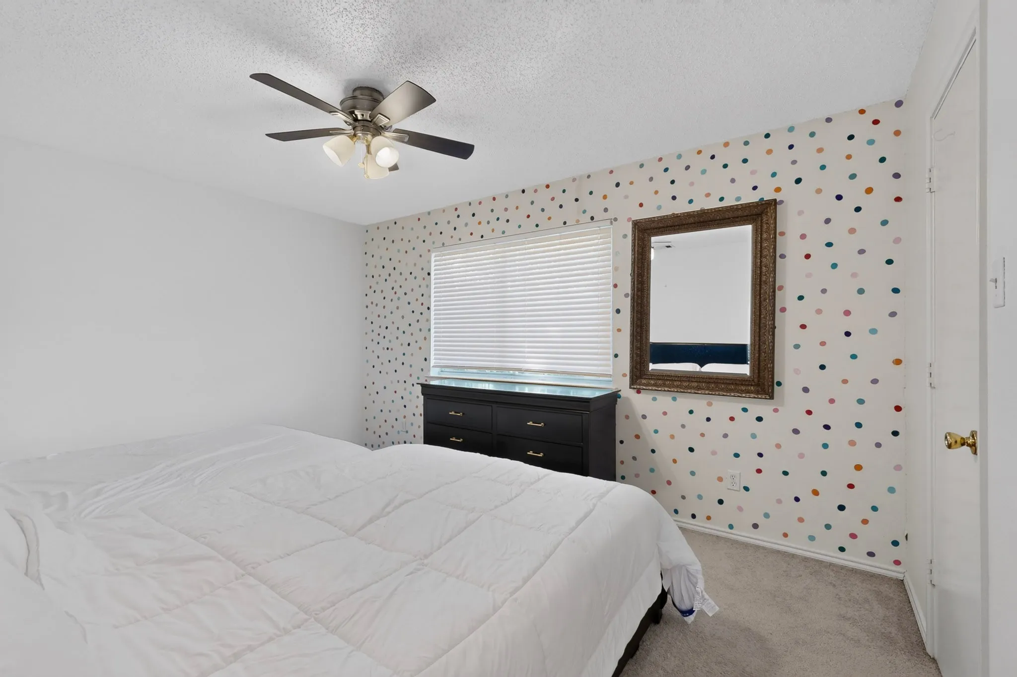 Ceiling fan with integrated lighting, window with blinds, wall-mounted mirror, and wall featuring patterned accents