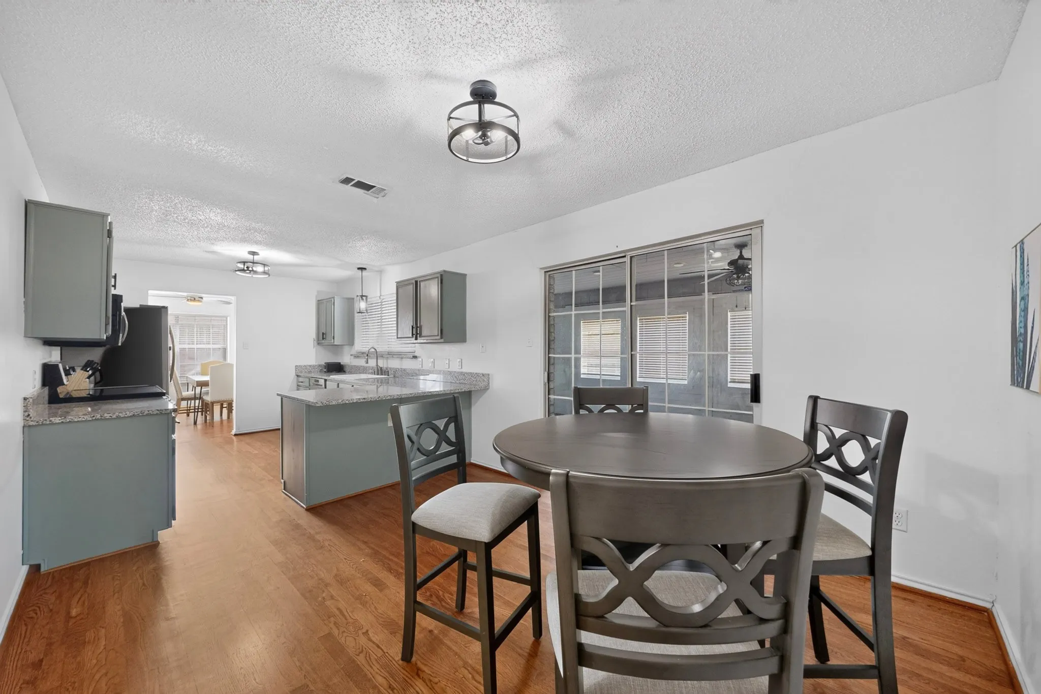 Kitchen and dining area featuring wood-finish flooring, granite countertops, gray cabinetry, and a sliding glass door
