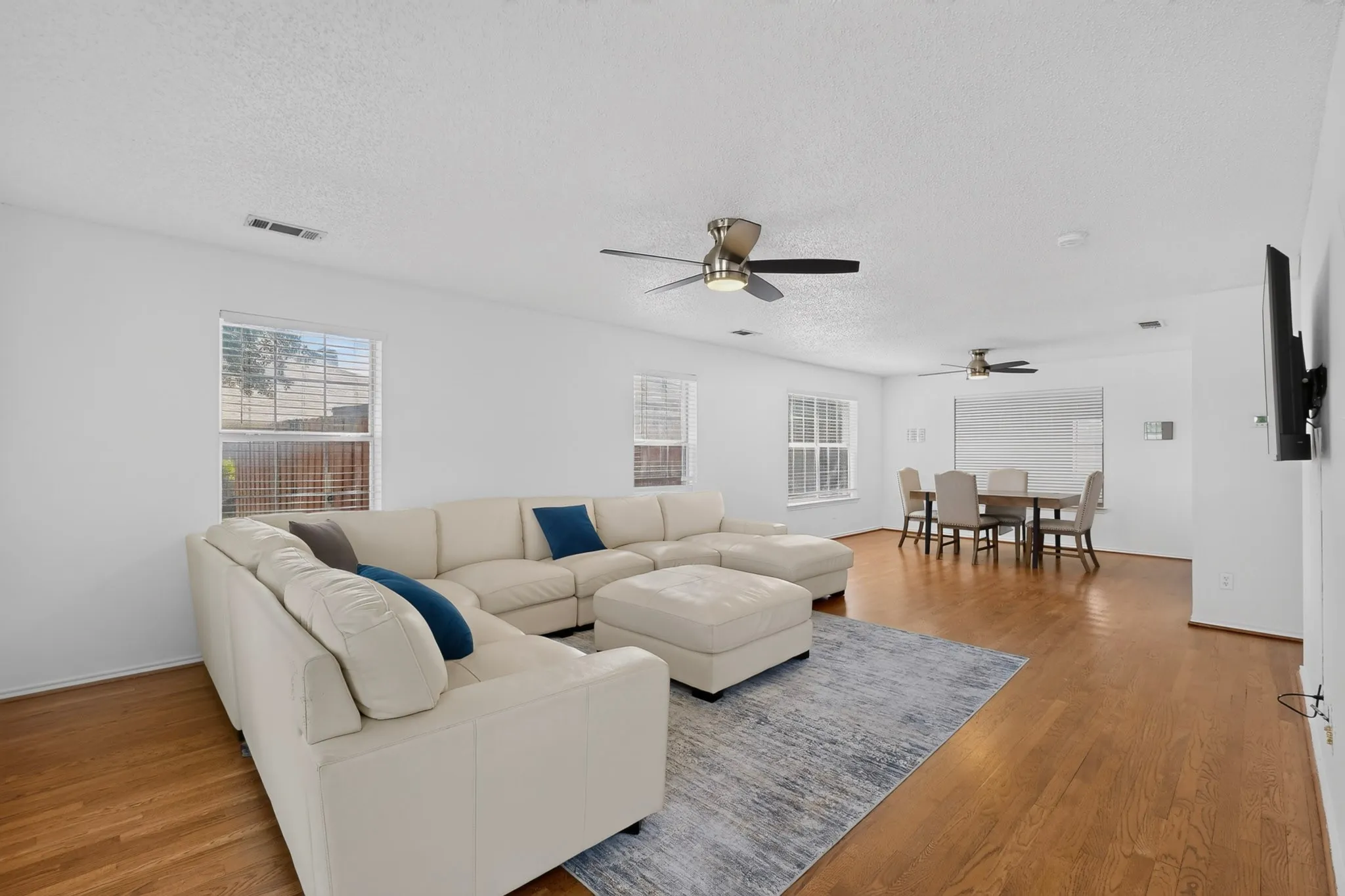 Hardwood-style flooring throughout, multiple windows with blinds, and two ceiling fans with integrated lighting