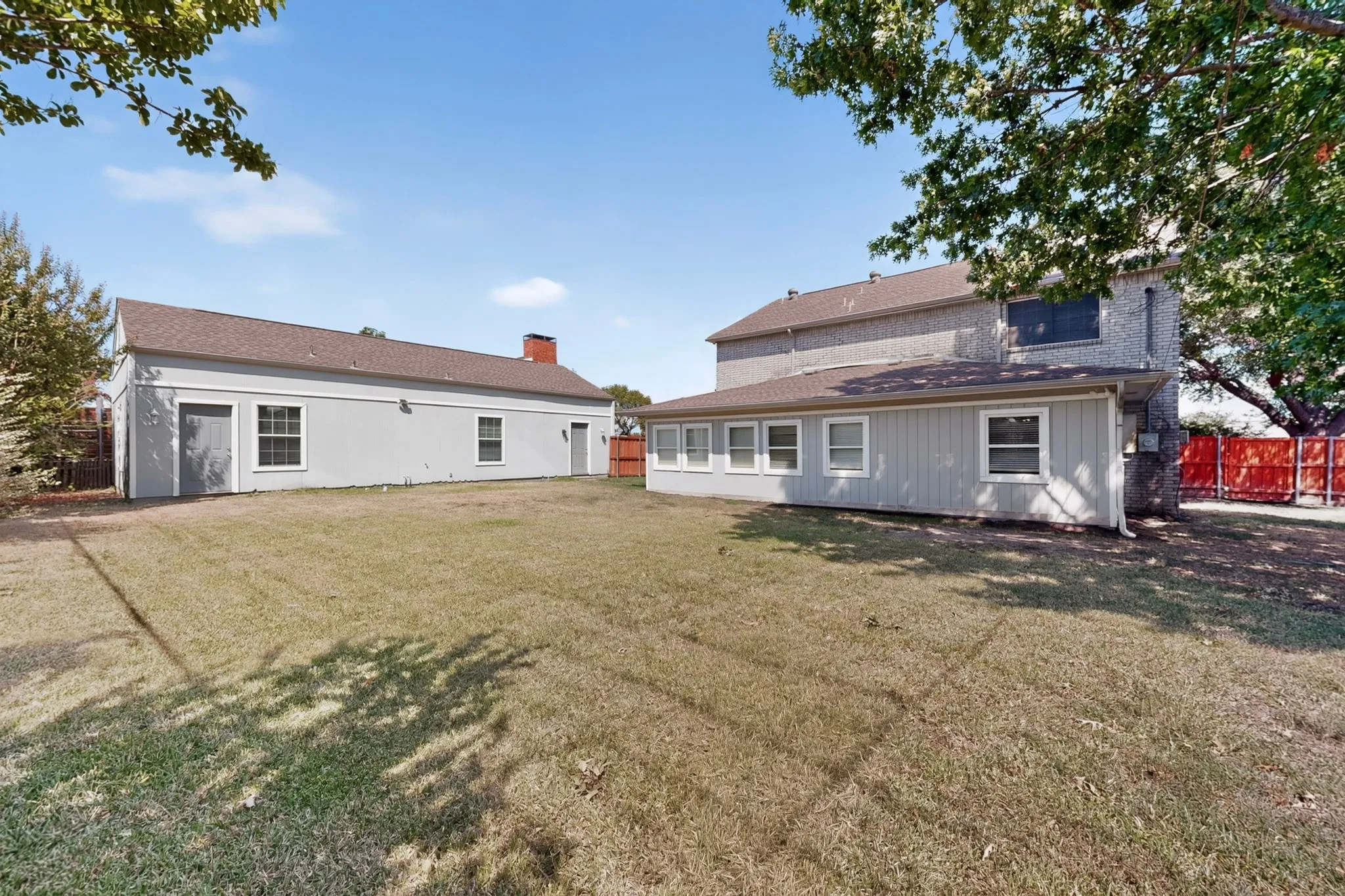 Expansive grassy area with a detached structure featuring multiple entry points and windows, alongside a property with a brick and siding exterior, offering multiple windows