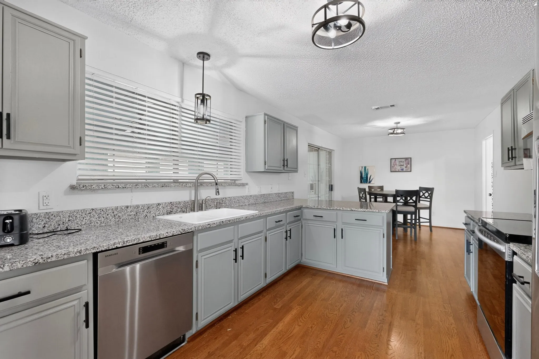 Galley kitchen featuring wood-finish flooring, light gray cabinetry, stainless steel appliances, and granite-style countertops