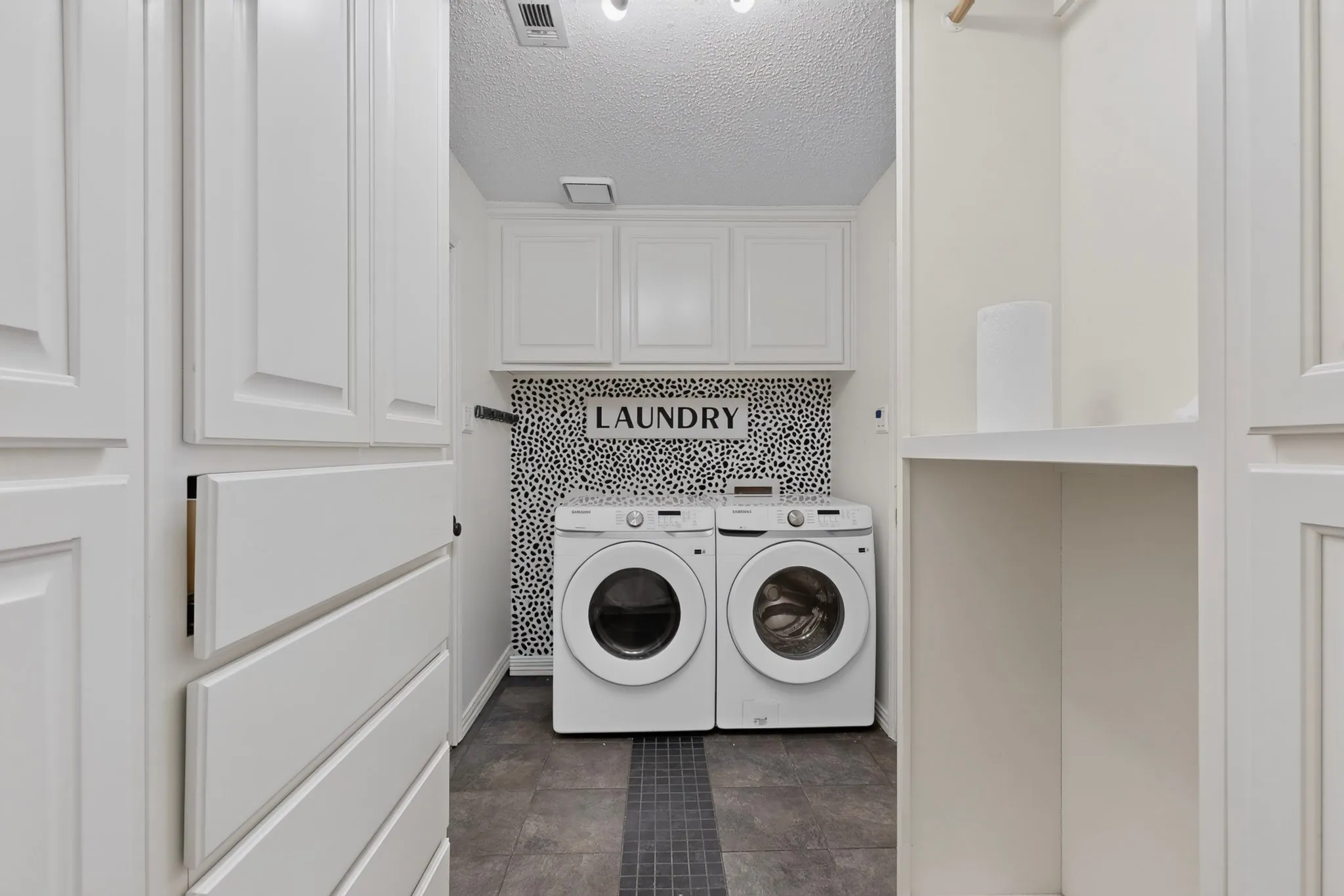 Laundry area featuring white cabinetry, built-in shelving, patterned tile backsplash, and dark floor tiles