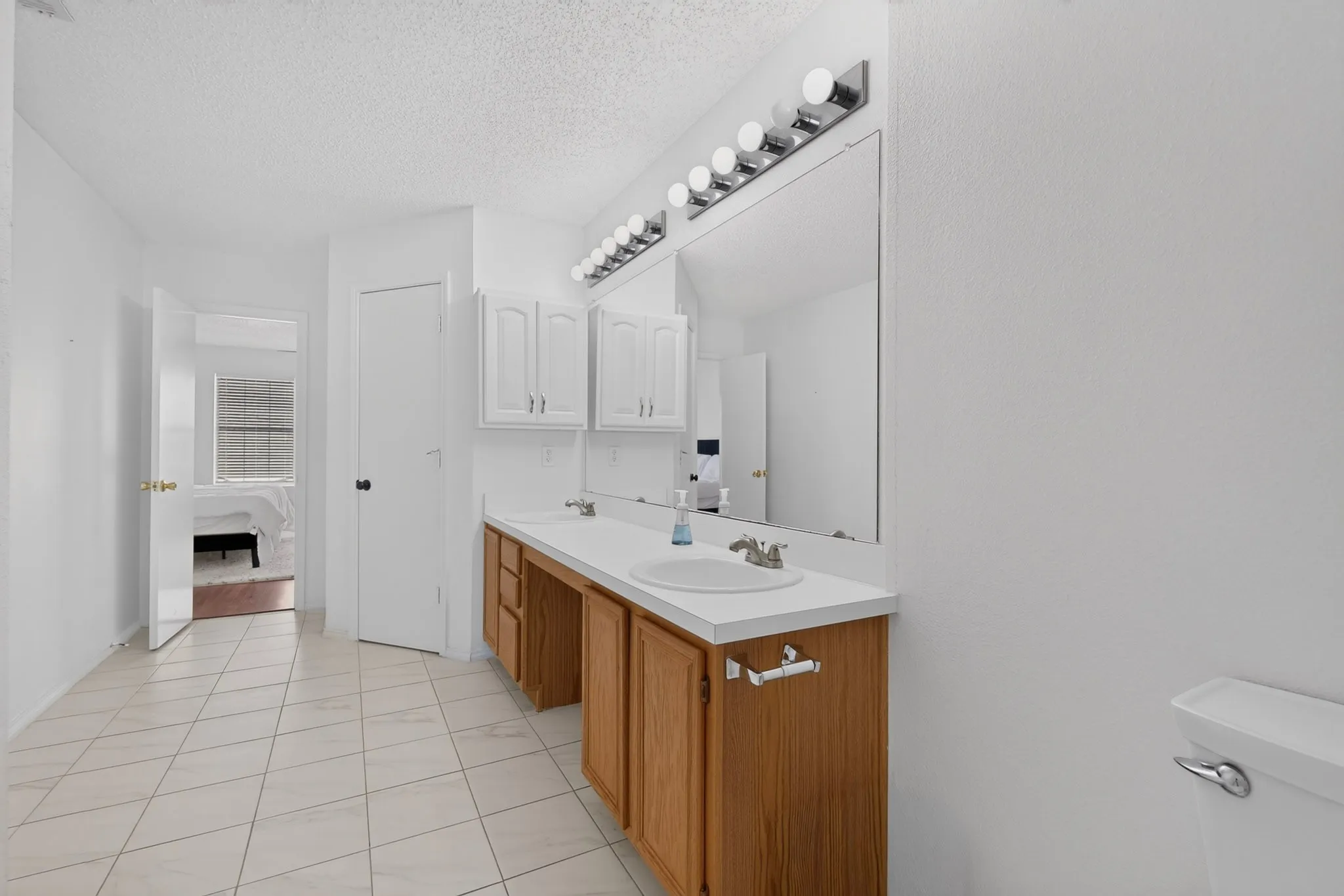 Double vanity with integrated sinks, wood-finish cabinetry, built-in storage, and wall-mounted lighting
