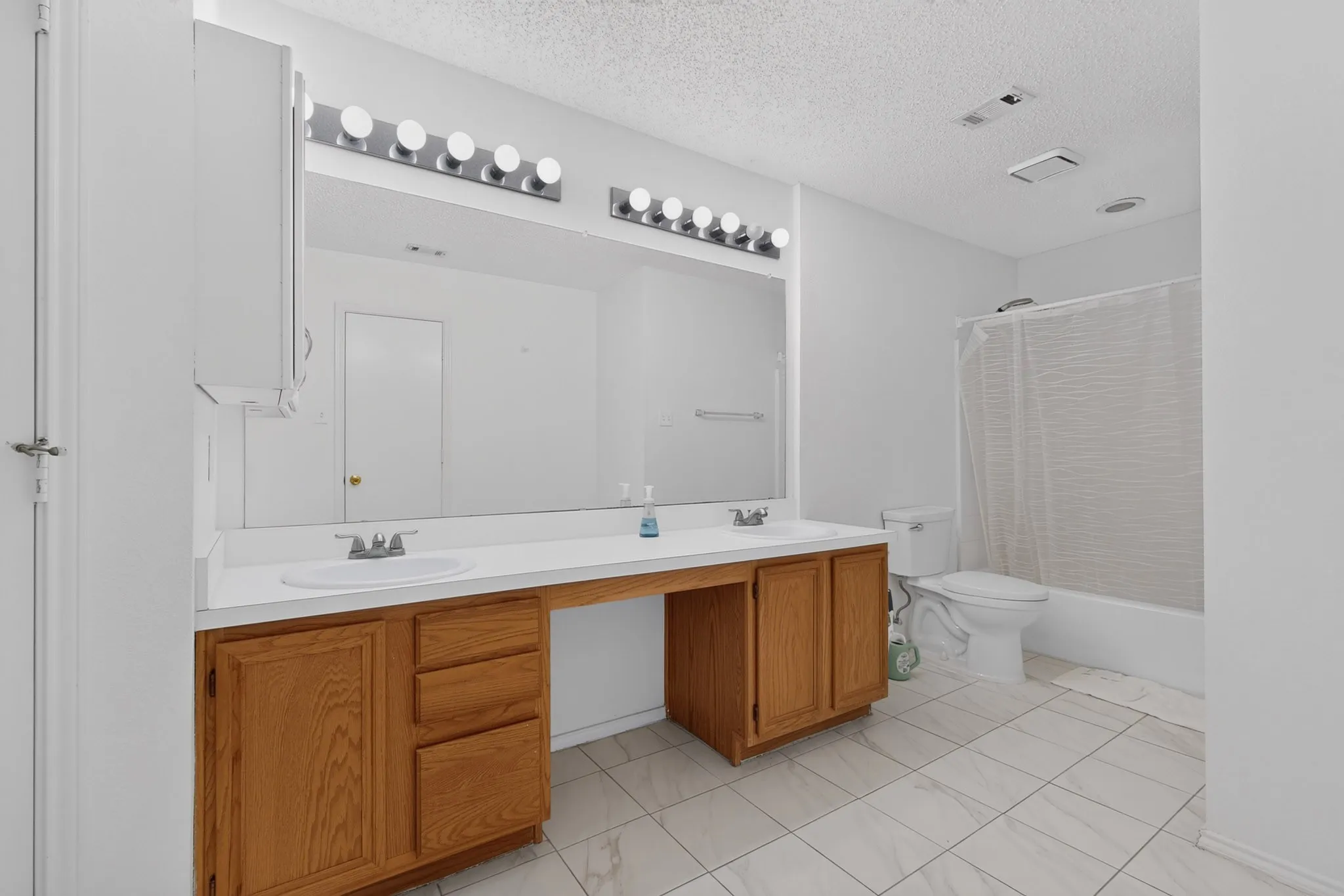 Dual sink vanity with wood-finish cabinetry, a large wall-mounted mirror, and tile flooring