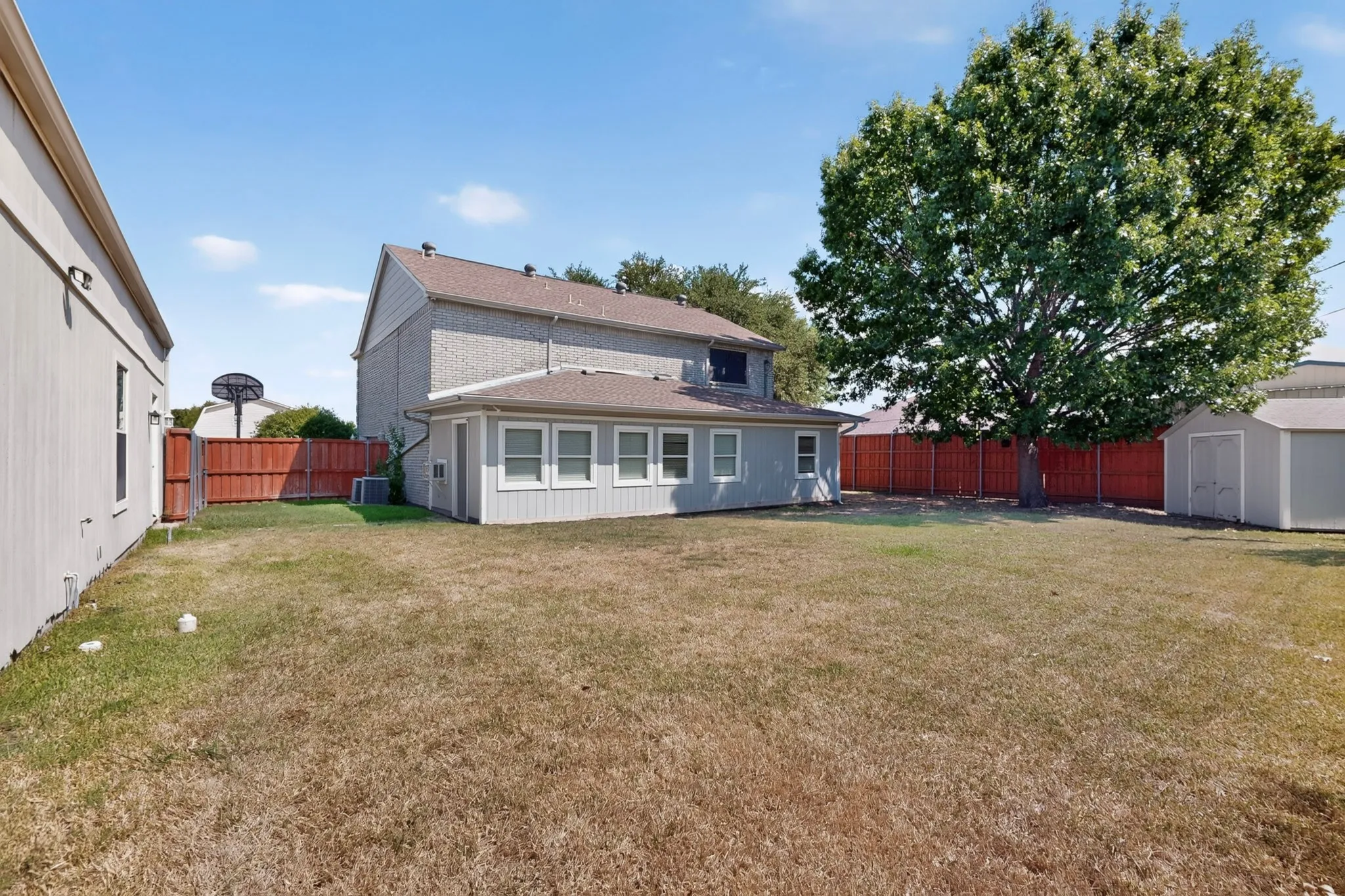 Expansive backyard featuring a mature tree, wooden privacy fencing, and two detached storage sheds