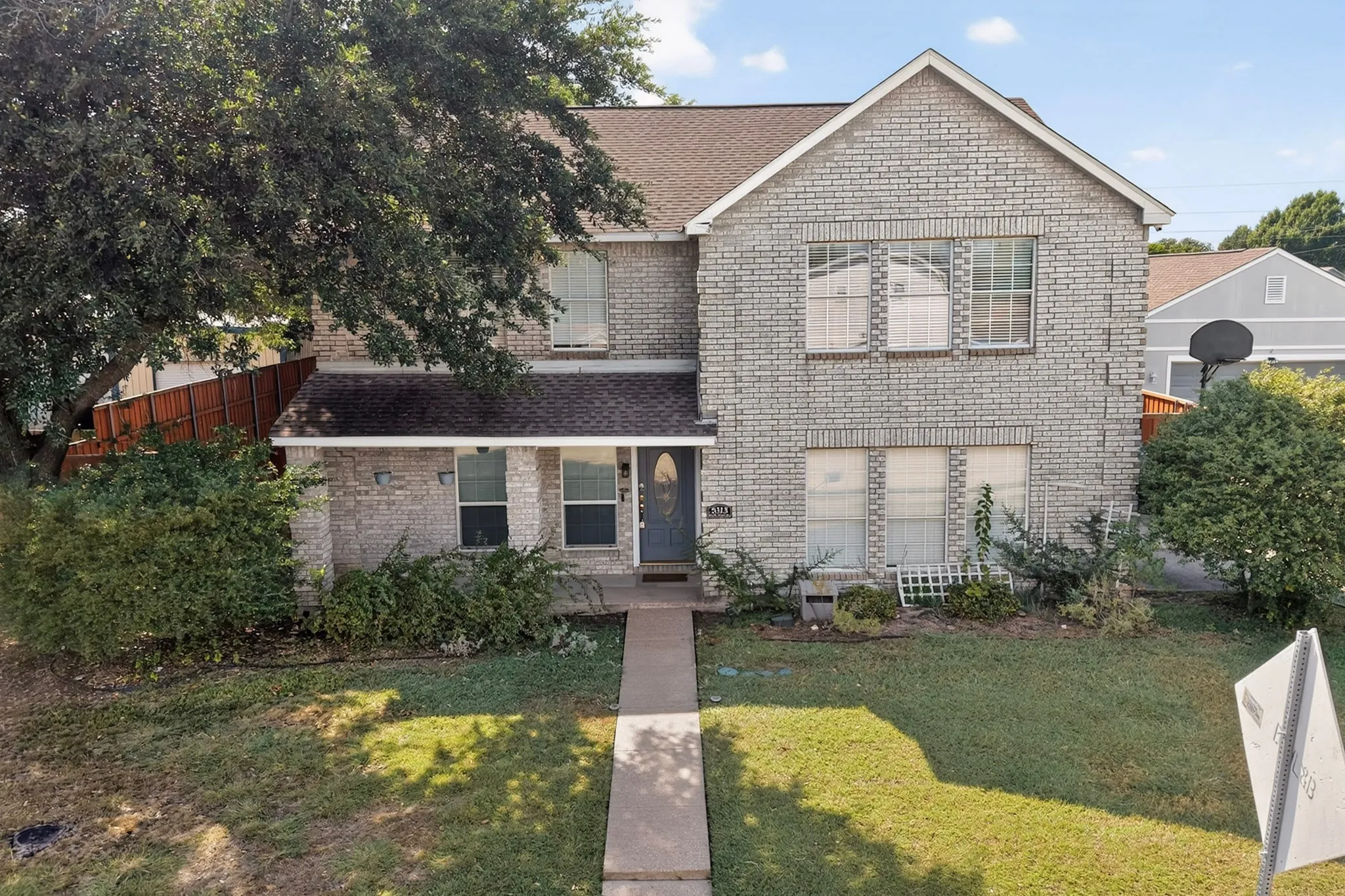 Two-story residence featuring a light brick exterior, a covered front entry, and a concrete walkway