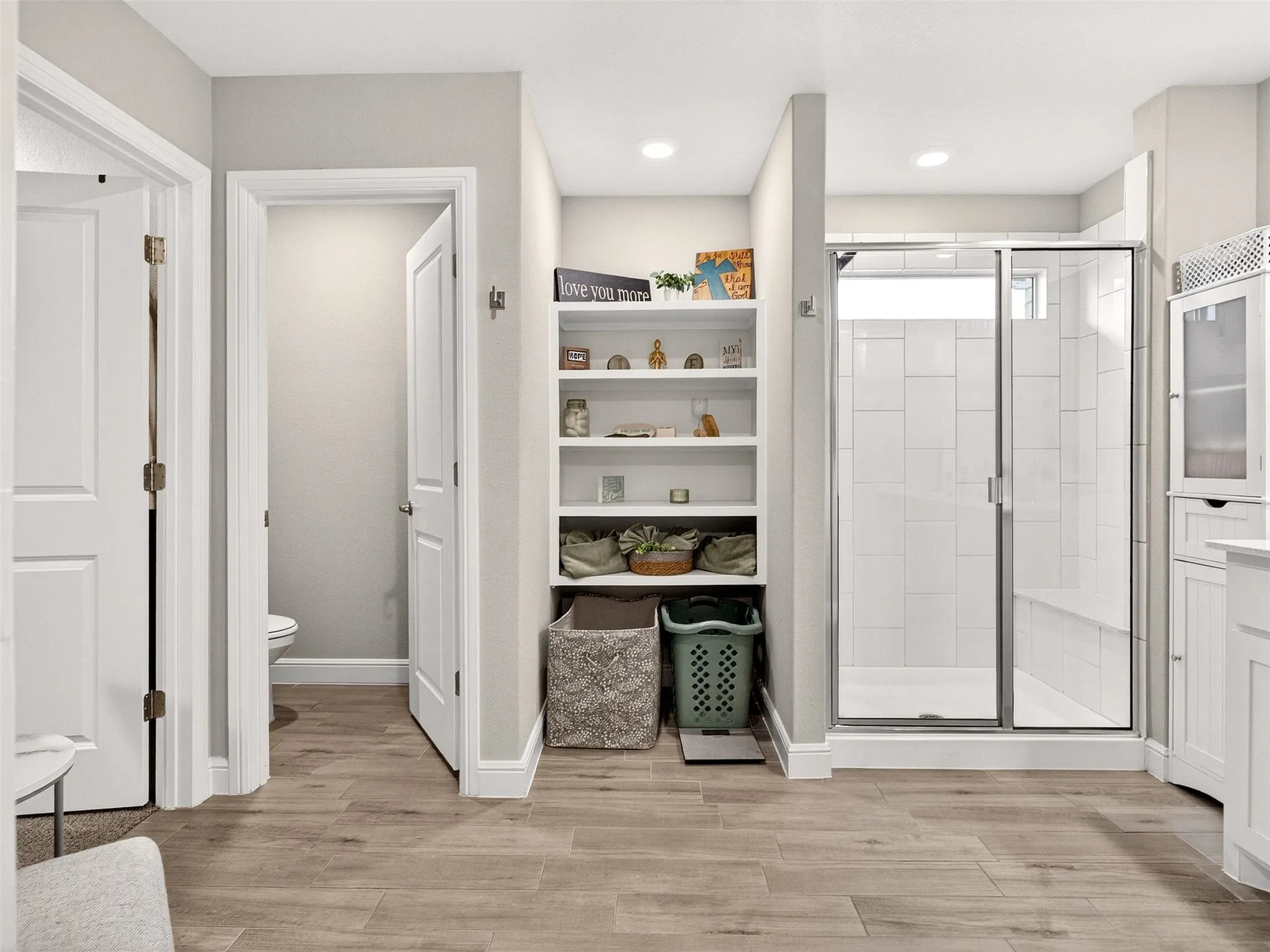 Recessed lighting, built-in shelving, glass-enclosed shower, white subway tile, and wood-finish flooring
