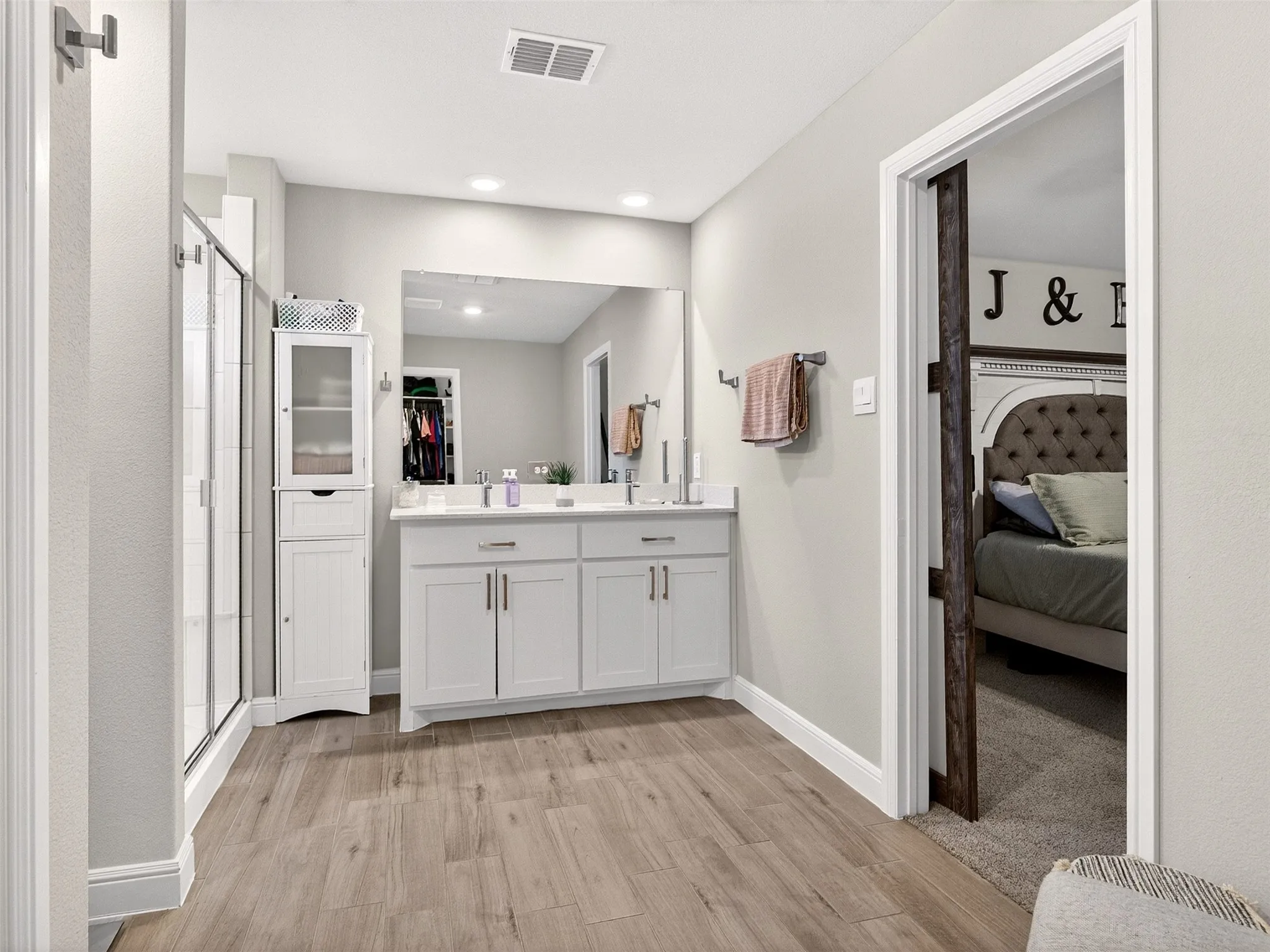 Dual vanity with undermount sinks, wood-finish flooring, recessed lighting, and a glass-enclosed shower