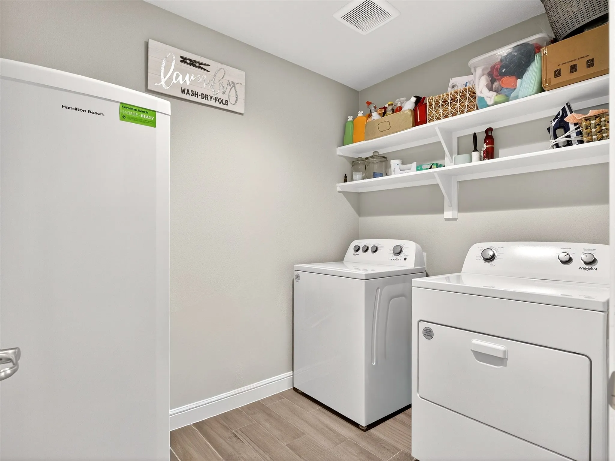 Laundry area featuring a top-load washer, front-load dryer, and two wall-mounted storage shelves