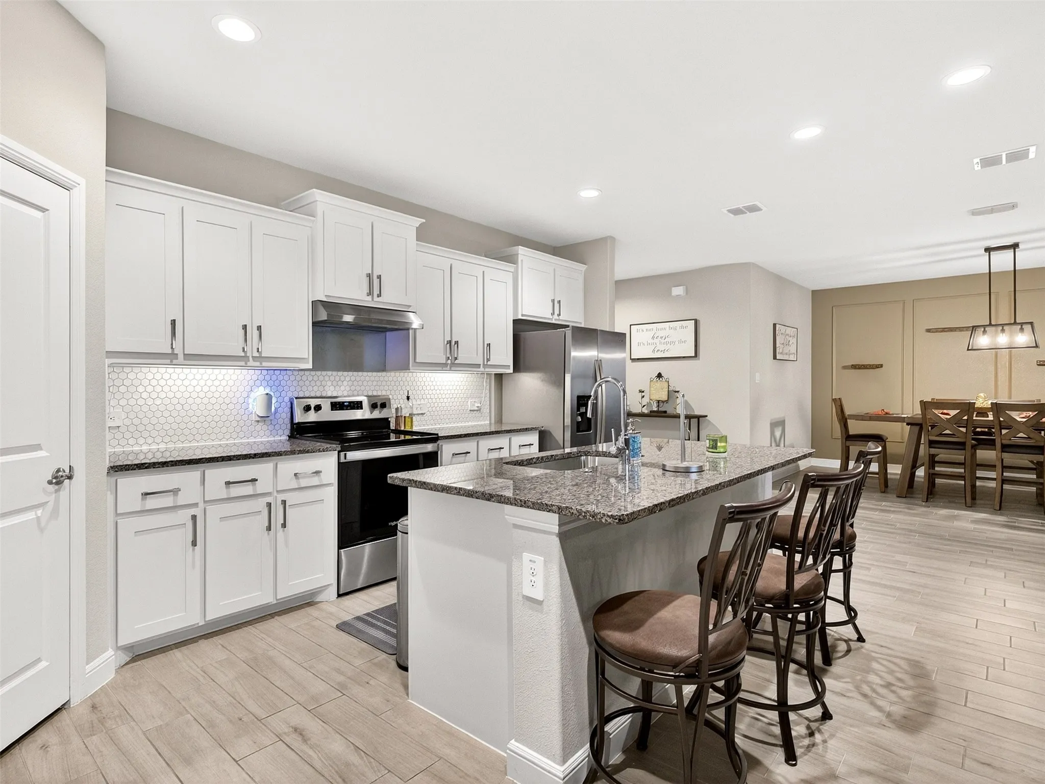 Open-concept kitchen featuring white cabinetry, a hexagonal tile backsplash, and a granite countertop island with a stainless steel sink