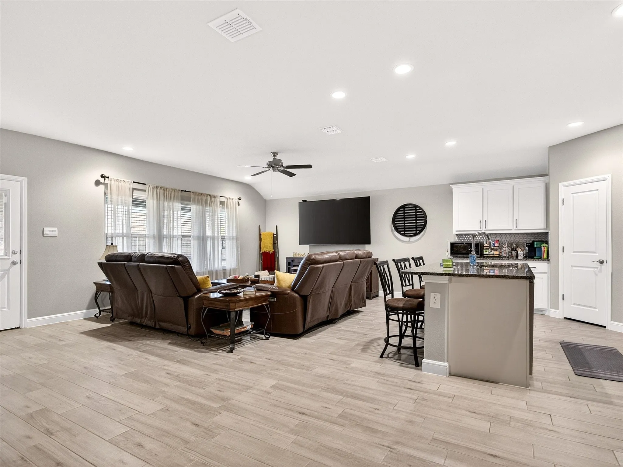 Open-concept living space featuring wood-finish flooring, recessed lighting, a vaulted ceiling with a ceiling fan, and white cabinetry with a built-in microwave