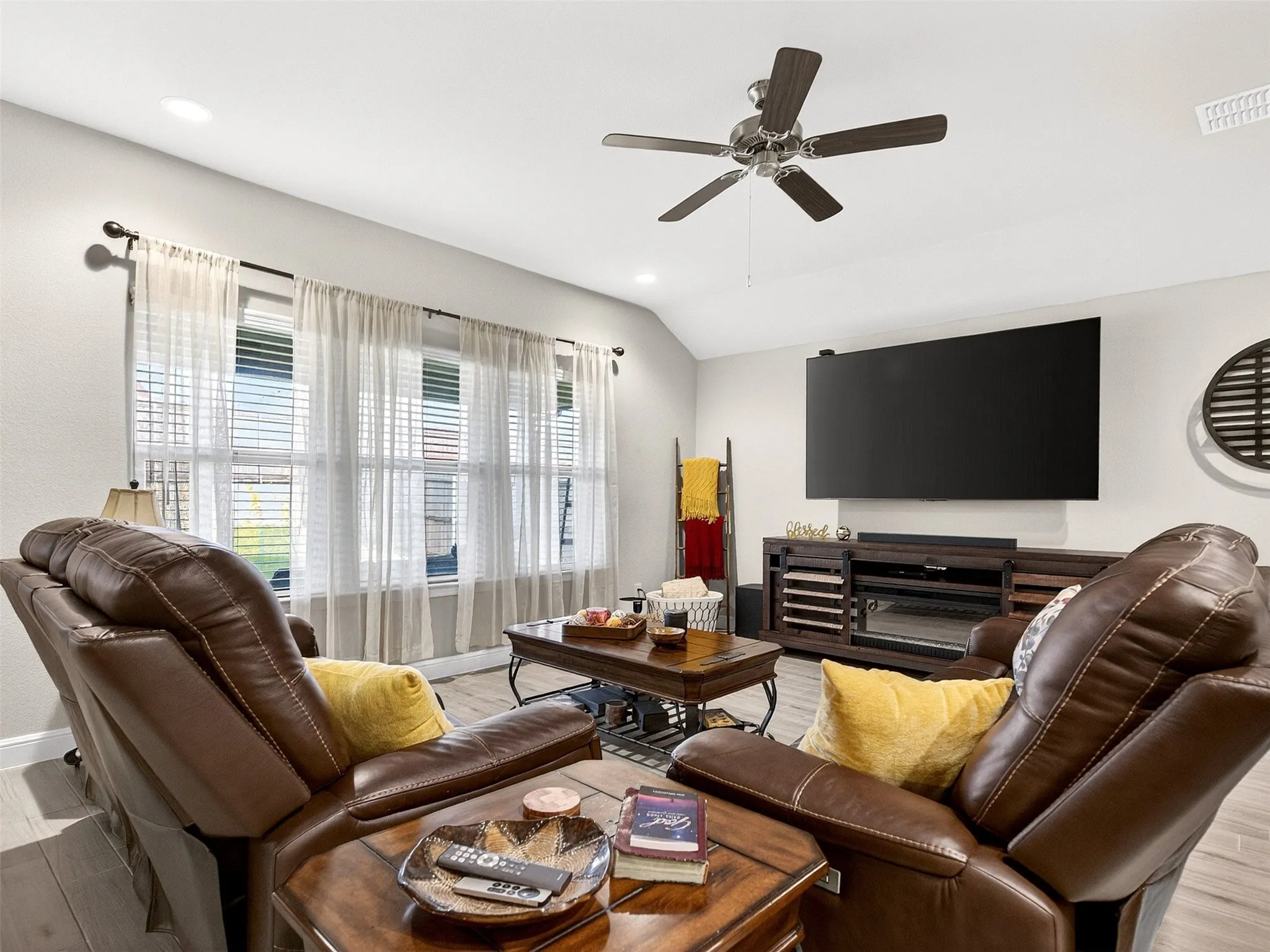 Vaulted ceilings, a ceiling fan with integrated lighting, recessed lighting, wood-finish flooring, and multiple windows
