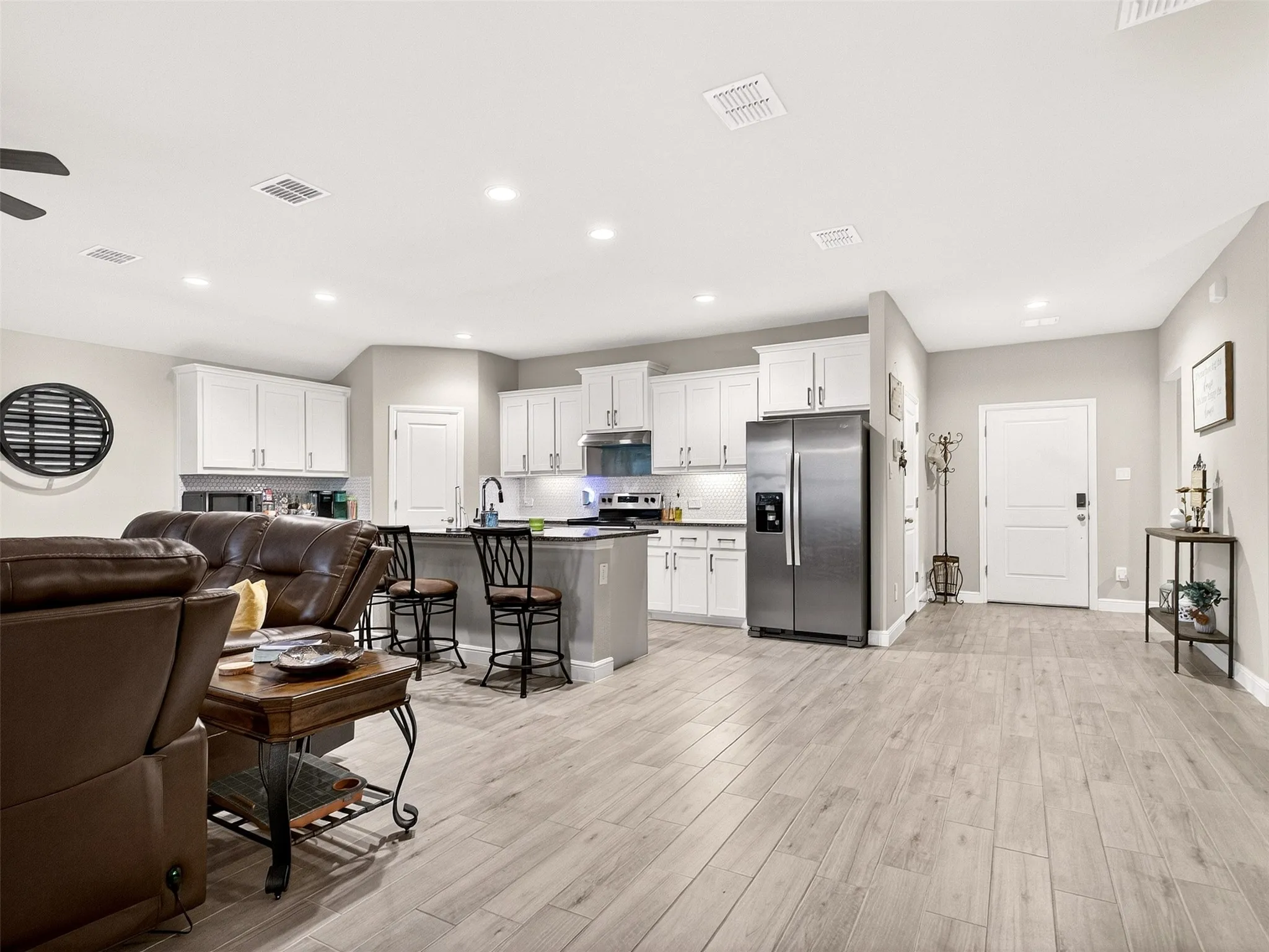 Open-concept living space featuring wood-finish flooring, recessed lighting, and a kitchen with white cabinetry and stainless steel appliances