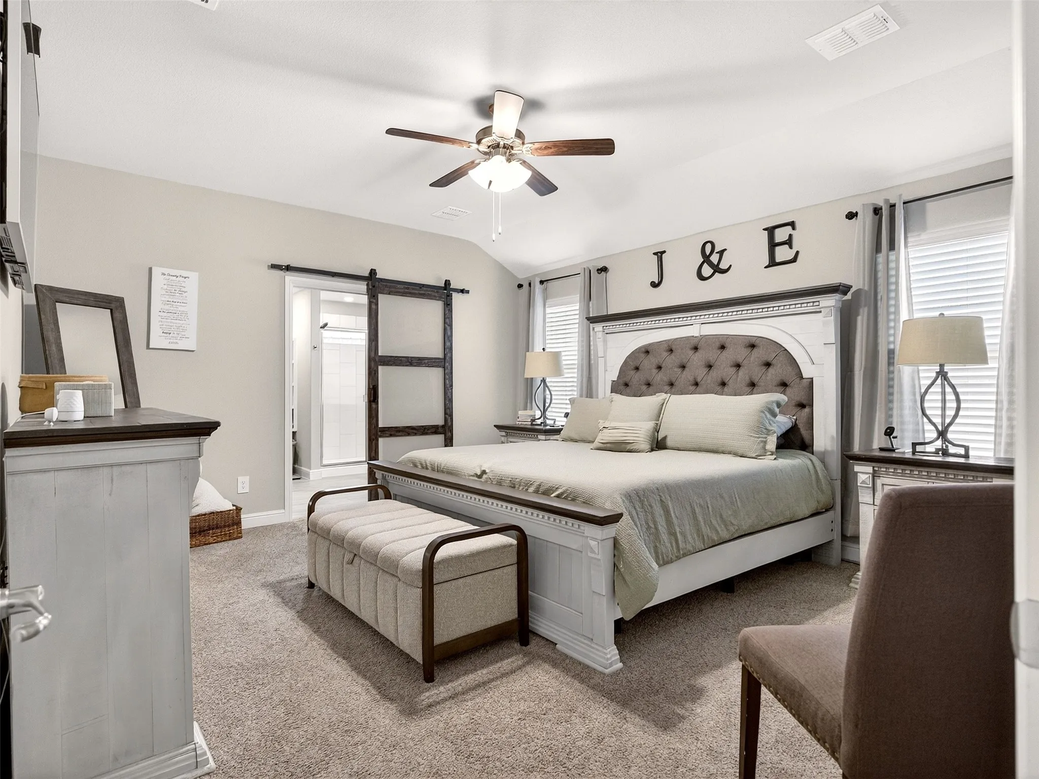 Vaulted ceiling with a ceiling fan, carpet flooring, dual windows with blinds, and a sliding barn door