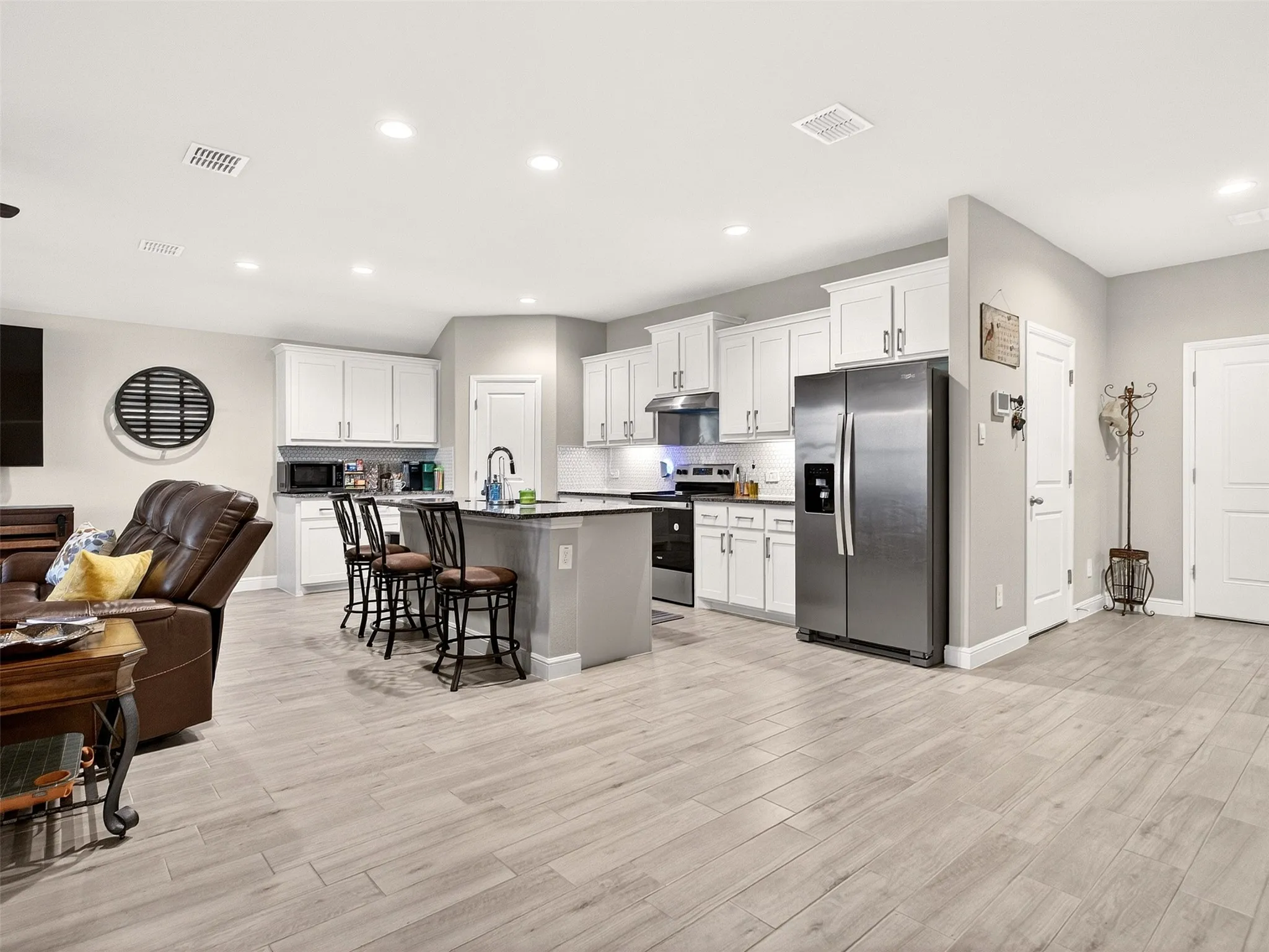 Open-concept living area with light-toned wood-finish flooring, recessed lighting, and a modern kitchen
