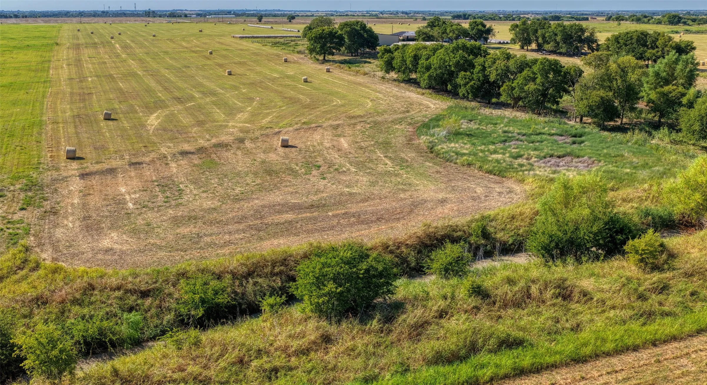 Expansive agricultural land featuring cultivated fields, natural waterways, and mature trees