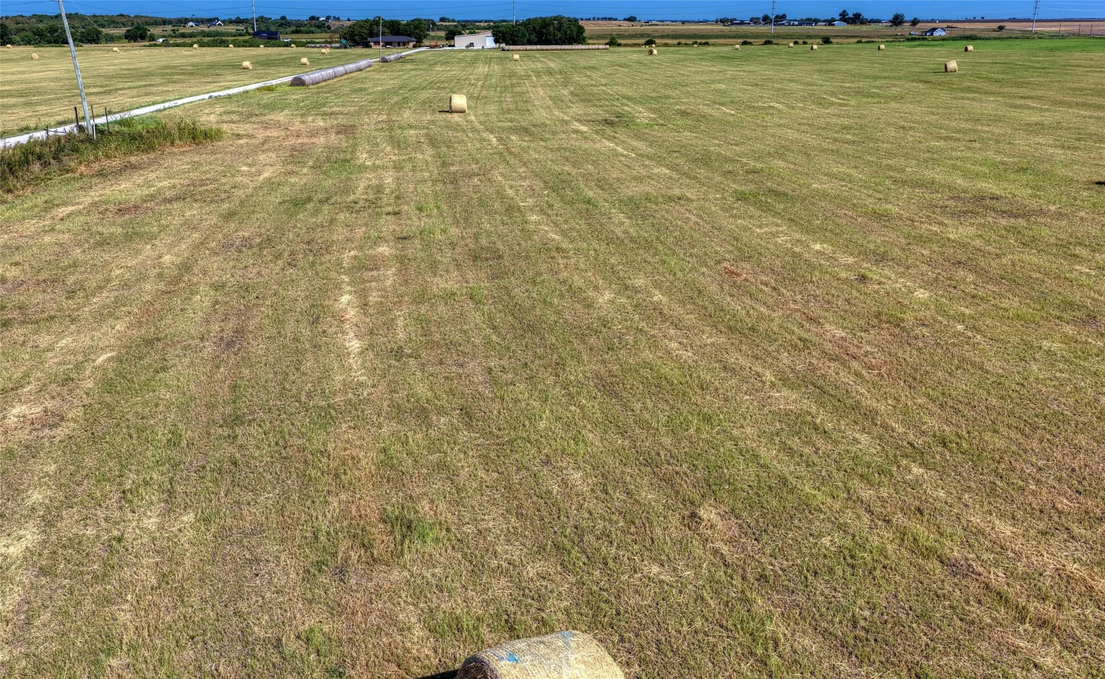 Expansive agricultural land featuring a gravel road, distant structures, and open fields