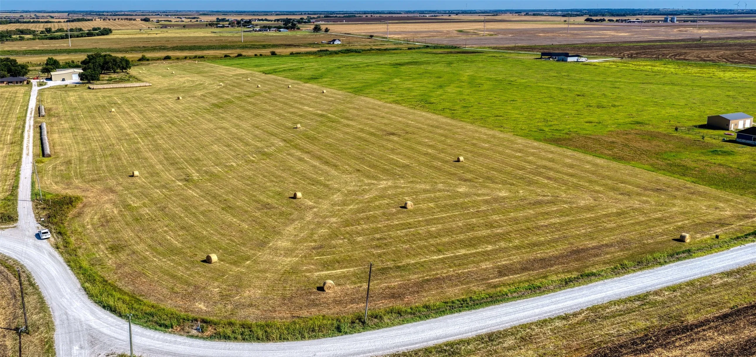 Expansive agricultural property featuring a gravel road, open fields, and distant structures