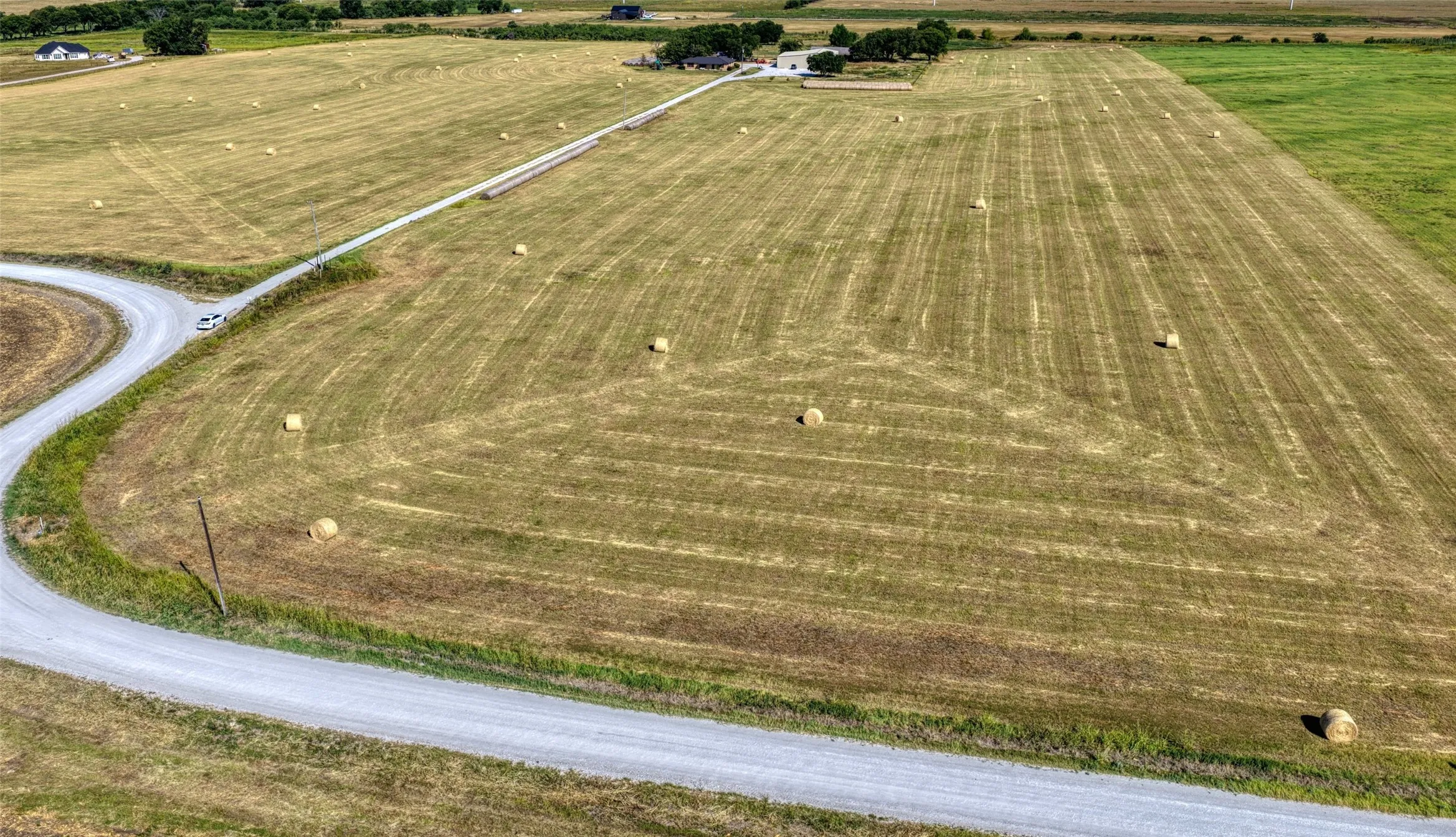 Expansive agricultural land featuring a gravel road and scattered hay bales