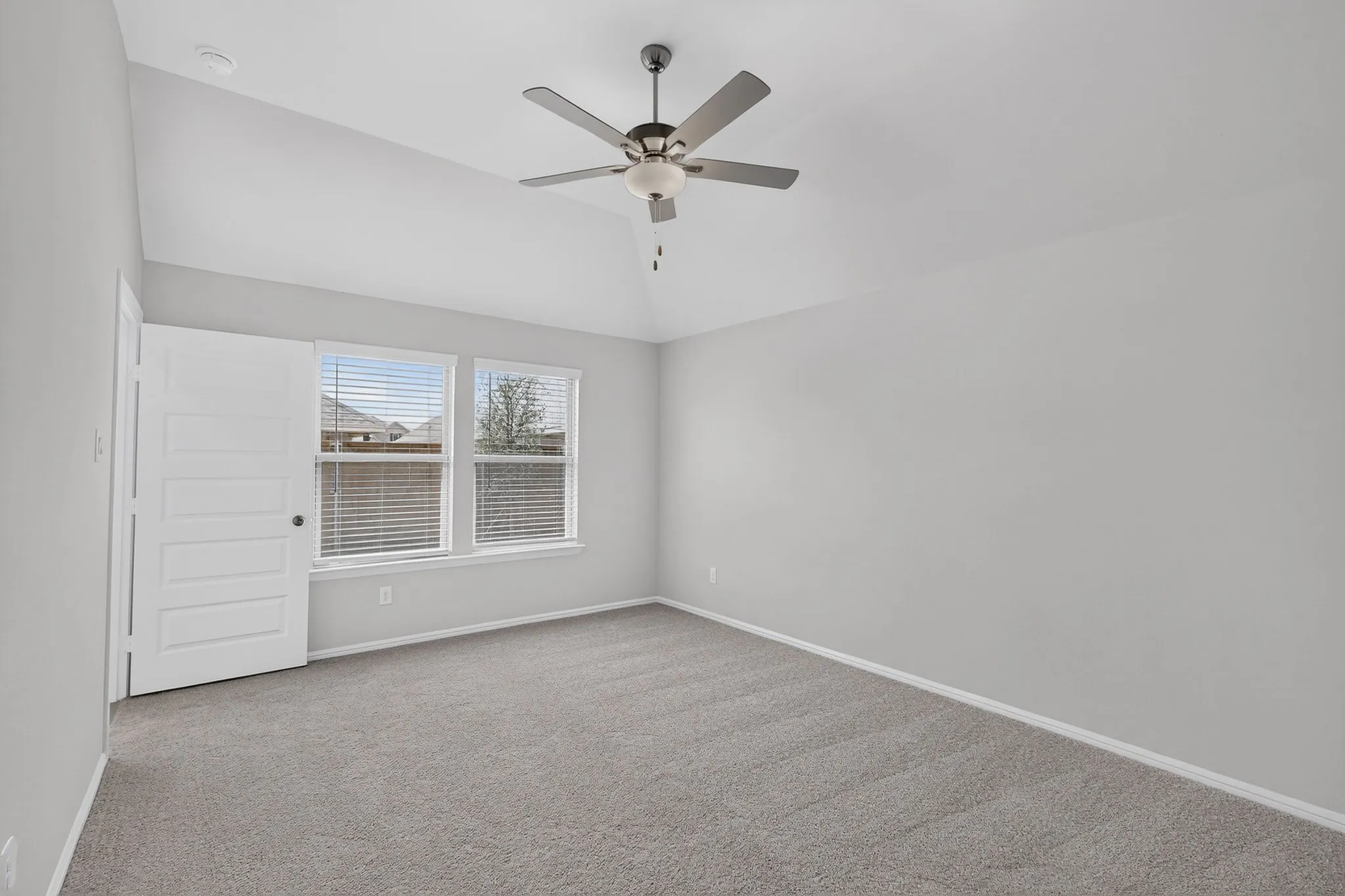 Vaulted ceiling with a ceiling fan, light gray wall finishes, gray carpeting, and two windows with blinds