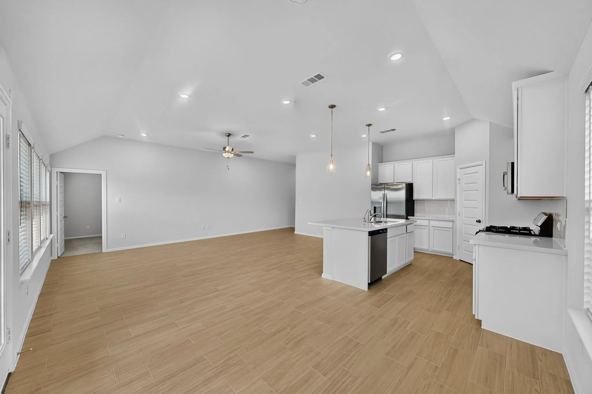 Vaulted ceiling with recessed lighting, wood-finish flooring, white cabinetry, stainless steel appliances, and a kitchen island with pendant lighting
