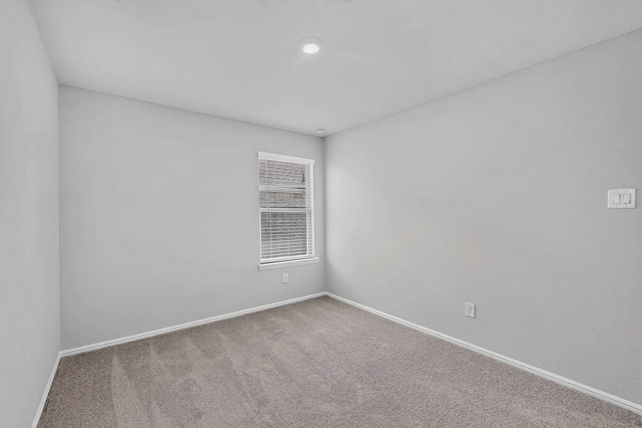 Recessed ceiling lighting, light gray wall paint, window with blinds, light gray carpeting