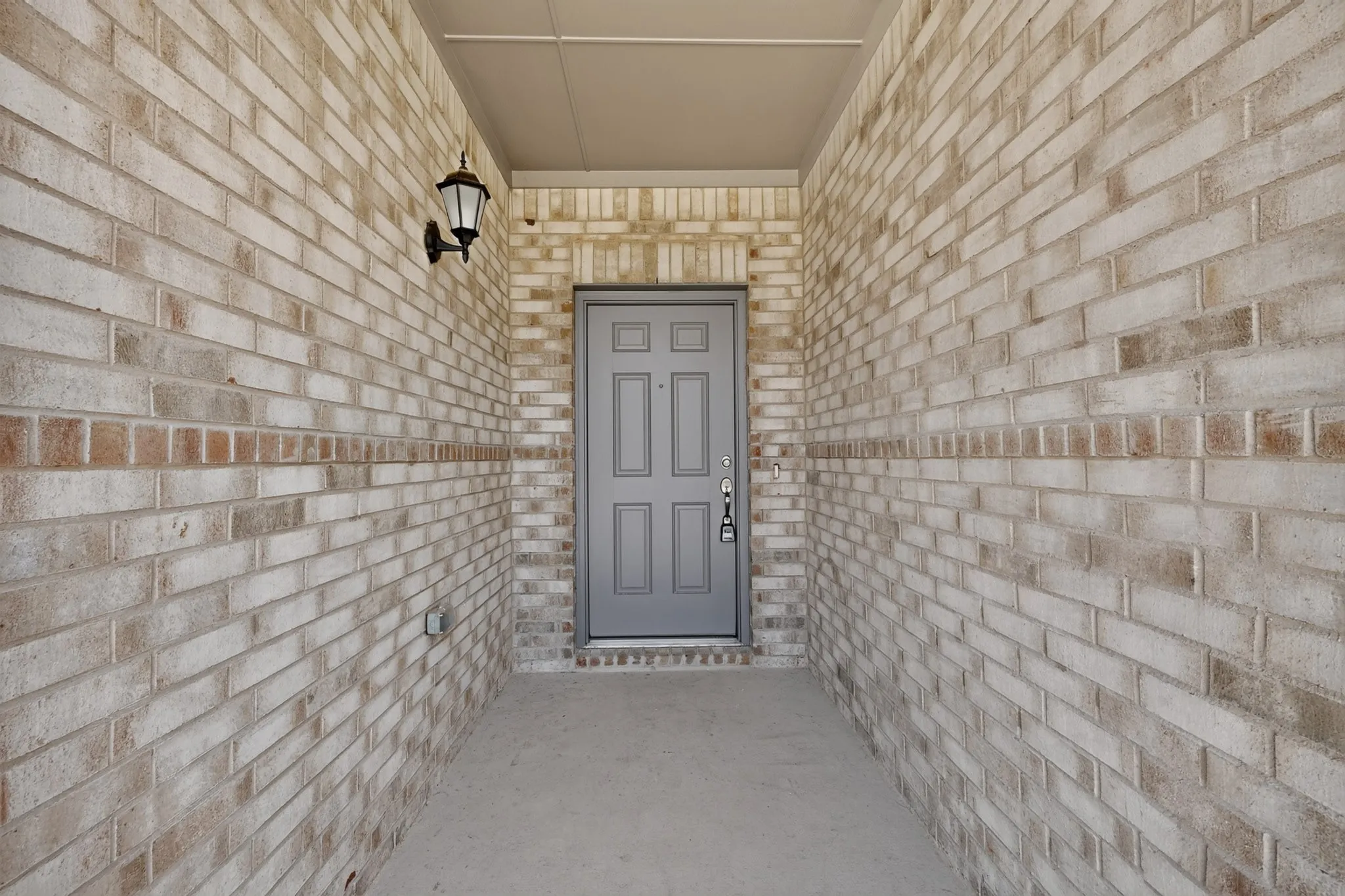 Recessed entry with a paneled door, brick exterior walls, and an exterior wall lantern