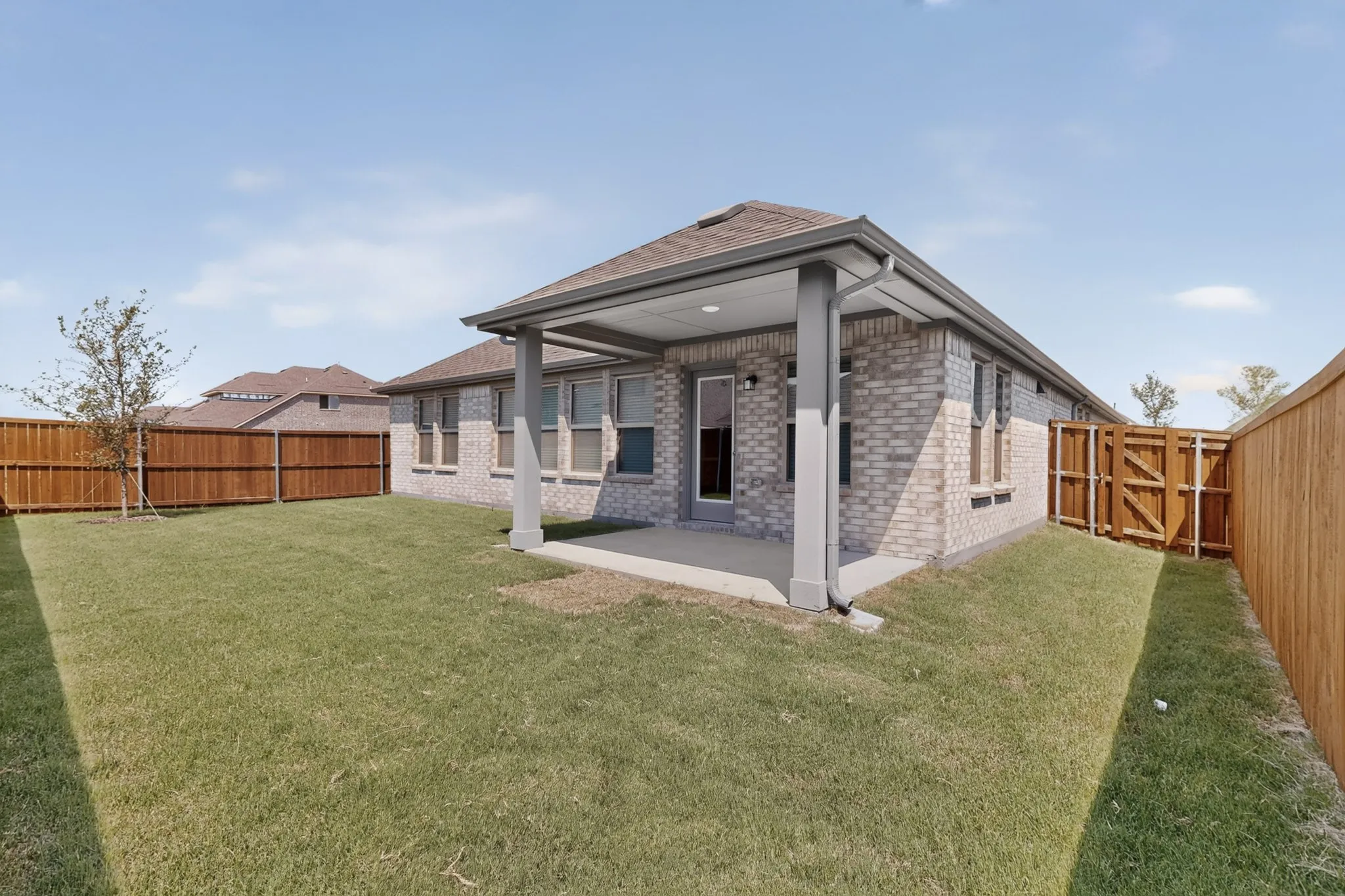 Covered concrete patio, brick exterior, full wood fencing, and a grassy lawn