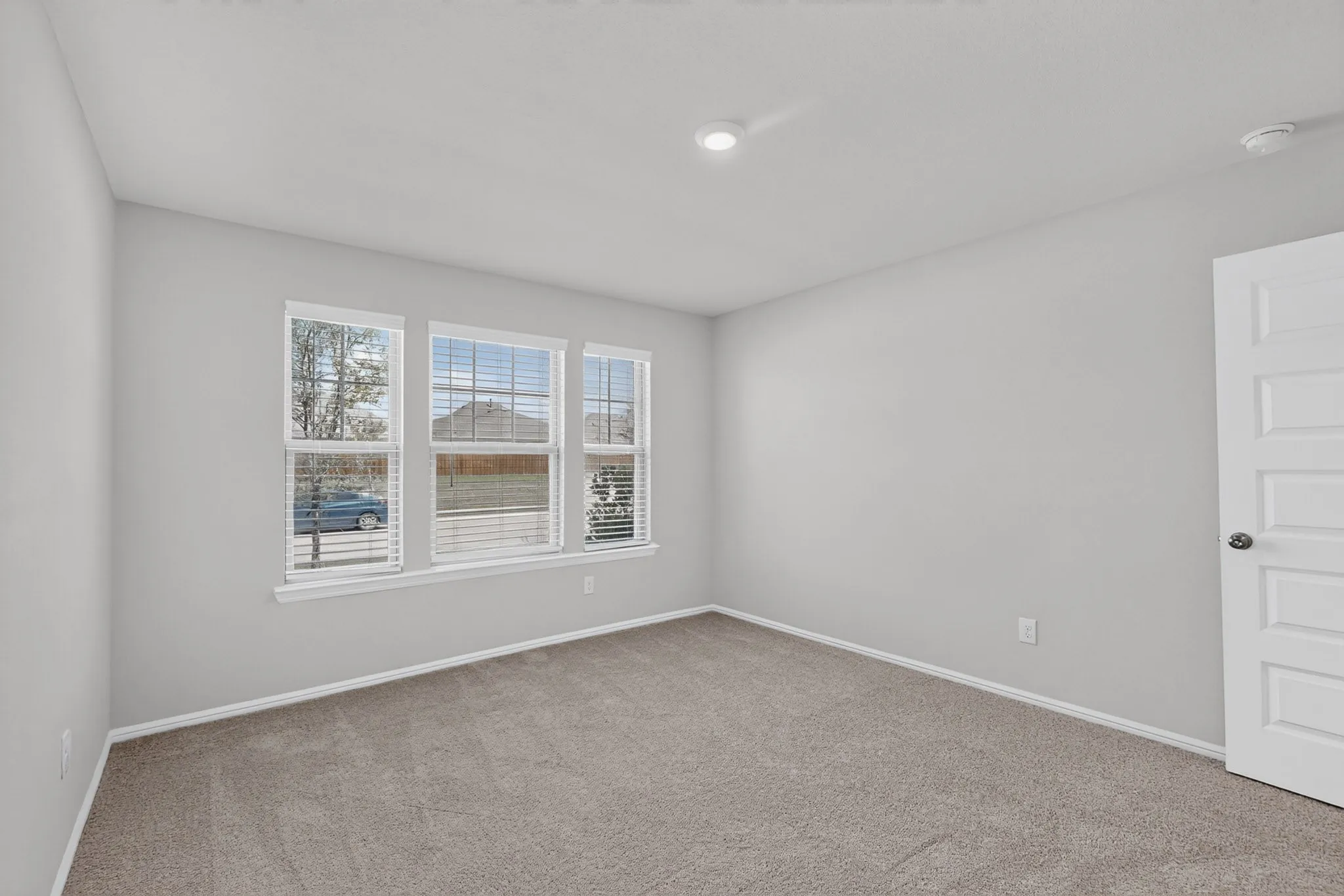 Carpeted flooring, three paneled windows with blinds, recessed ceiling lighting, and a five-panel interior door