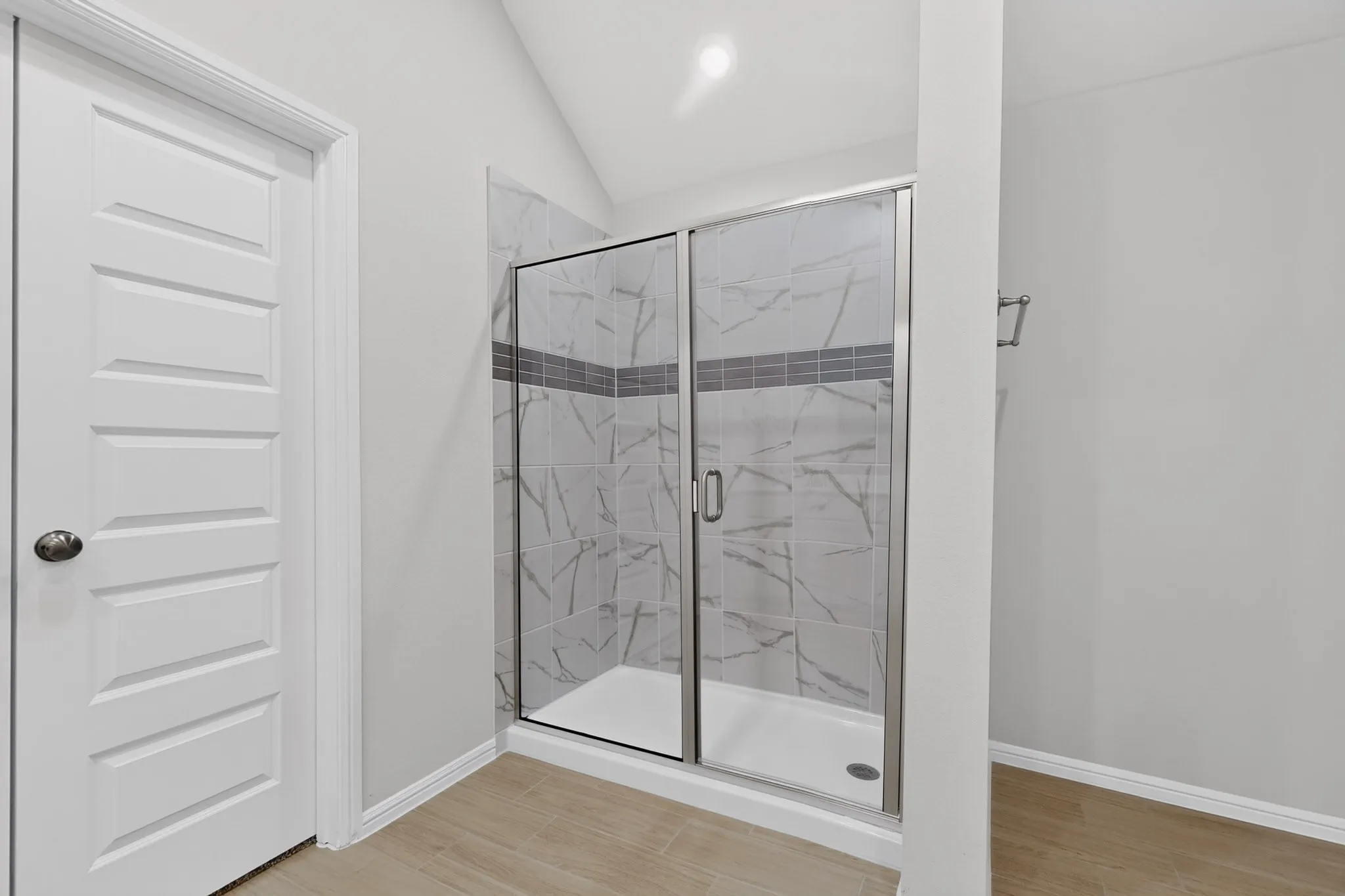 Shower enclosure with glass doors, white tiled walls featuring a gray accent band, and a white shower pan