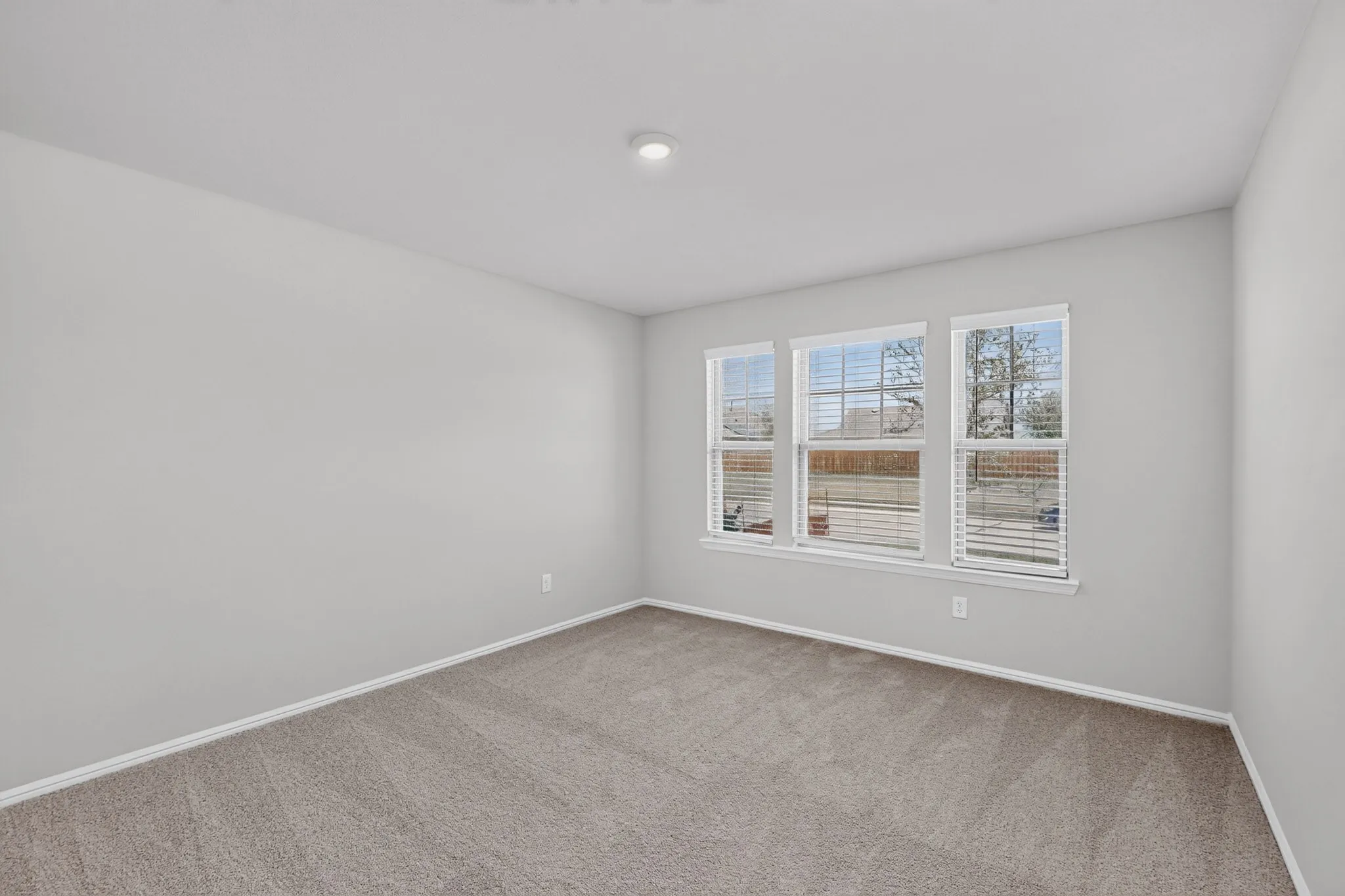 Carpeted flooring with light neutral wall tones, featuring three windows with blinds and a ceiling-mounted light fixture