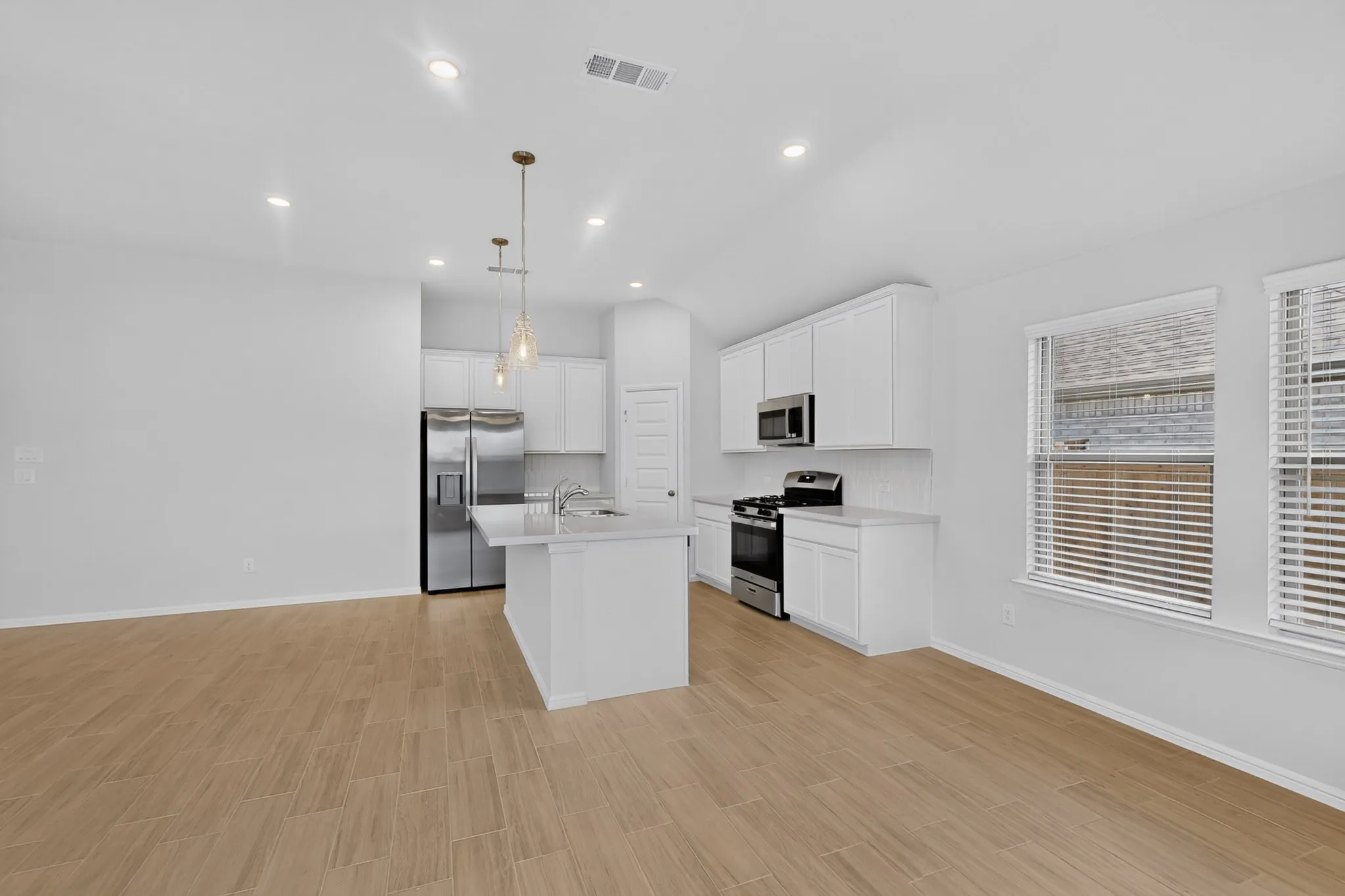 Kitchen featuring an island with built-in sink, stainless steel appliances, white cabinetry, and recessed lighting