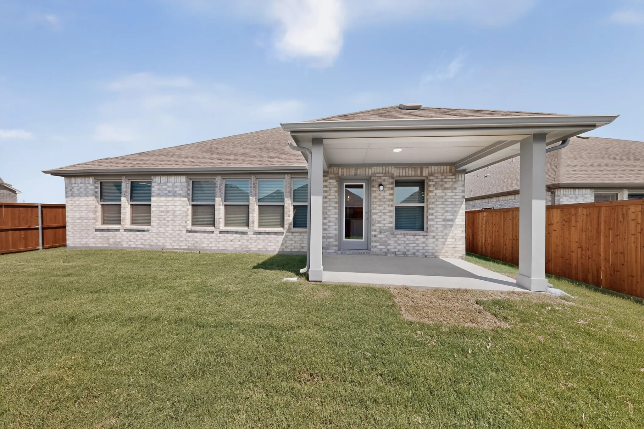 Covered patio with a concrete surface, light brick exterior, multiple windows, and a wood privacy fence