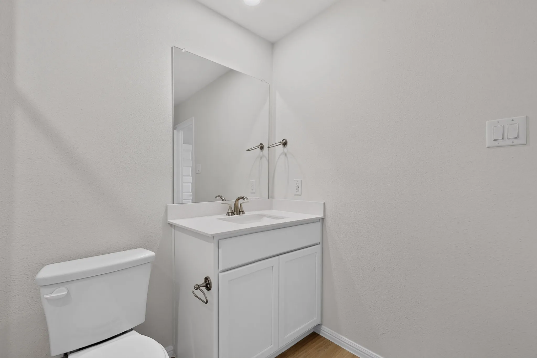 White vanity with a single basin sink, wall-mounted mirror, and wood-finish flooring