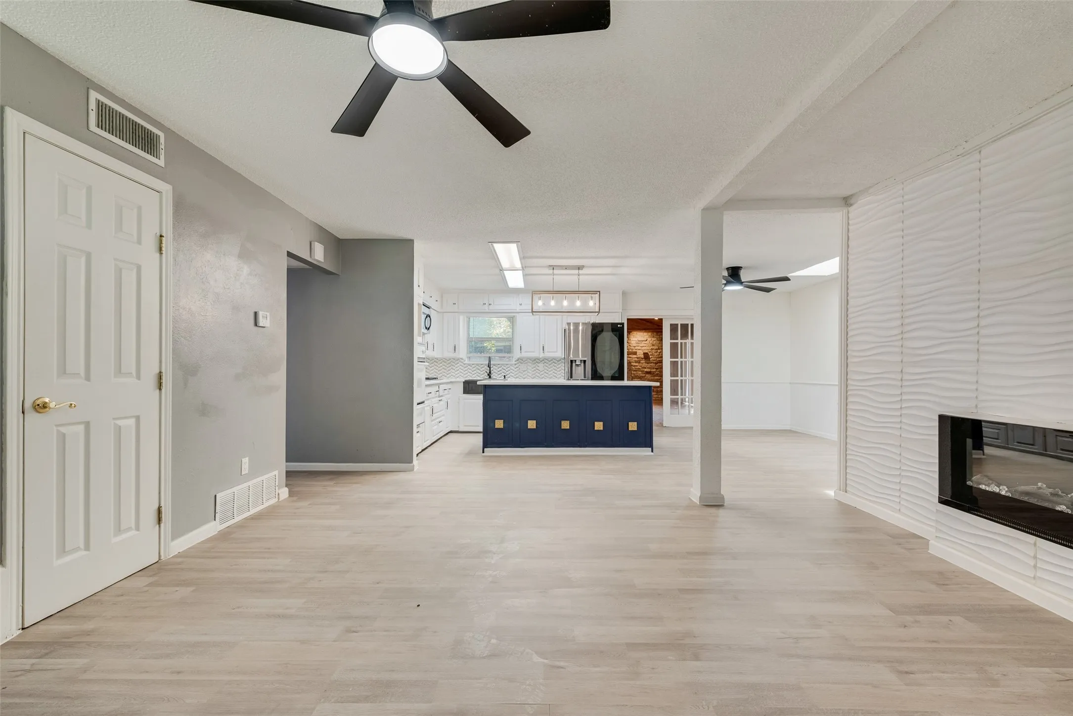 Open-concept layout featuring wood-finish flooring, a modern fireplace, white kitchen cabinetry, and a contrasting blue kitchen island