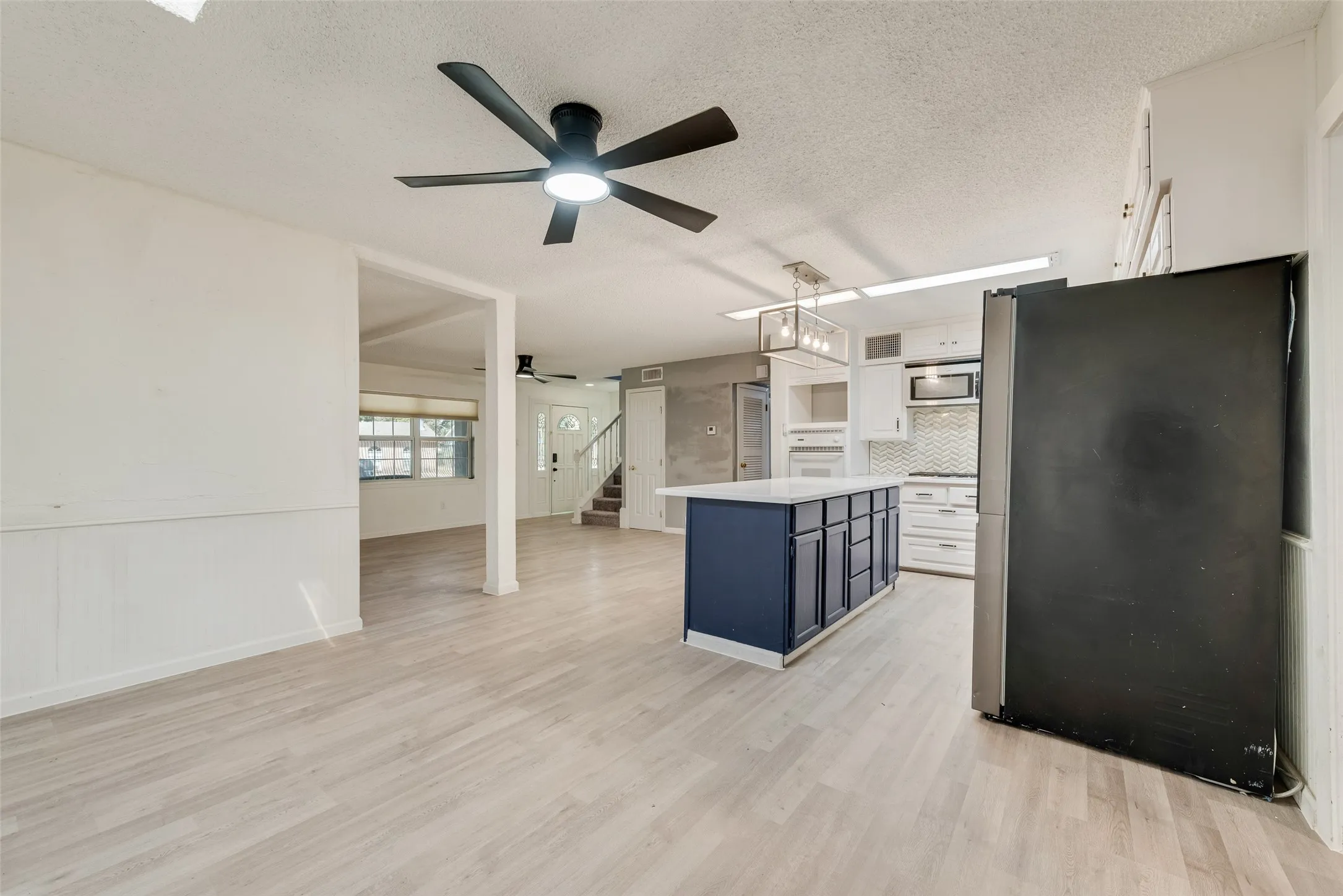 Wood-finish flooring throughout, kitchen island with built-in storage, white cabinetry, integrated stainless steel appliances, and ceiling fans with integrated lighting