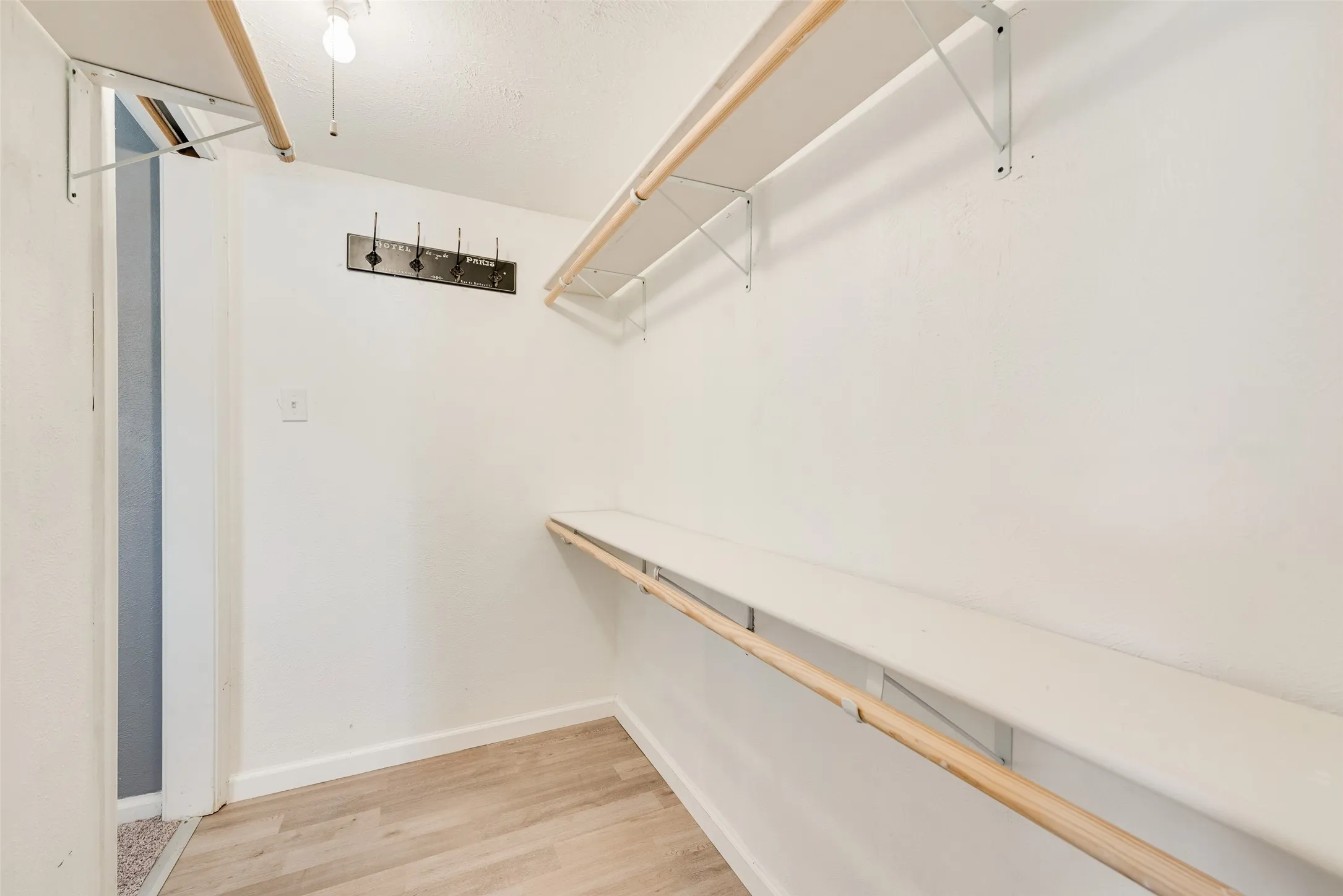 Wood-finish flooring with white baseboards, featuring white walls, a built-in hanging rod, and shelving