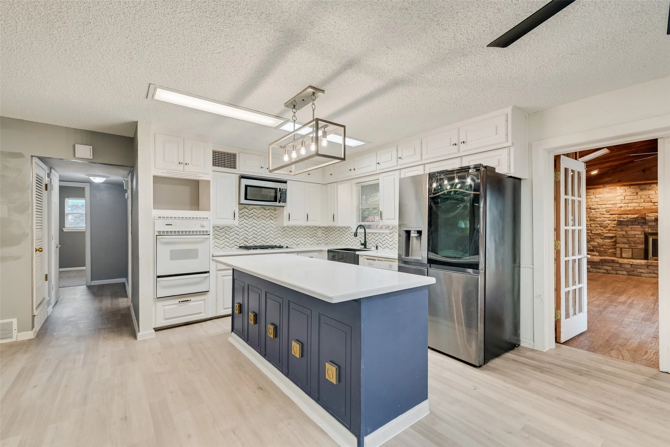 Kitchen featuring a central island with a white countertop and blue cabinetry, white upper and lower cabinetry, stainless steel appliances, and a chevron tile backsplash