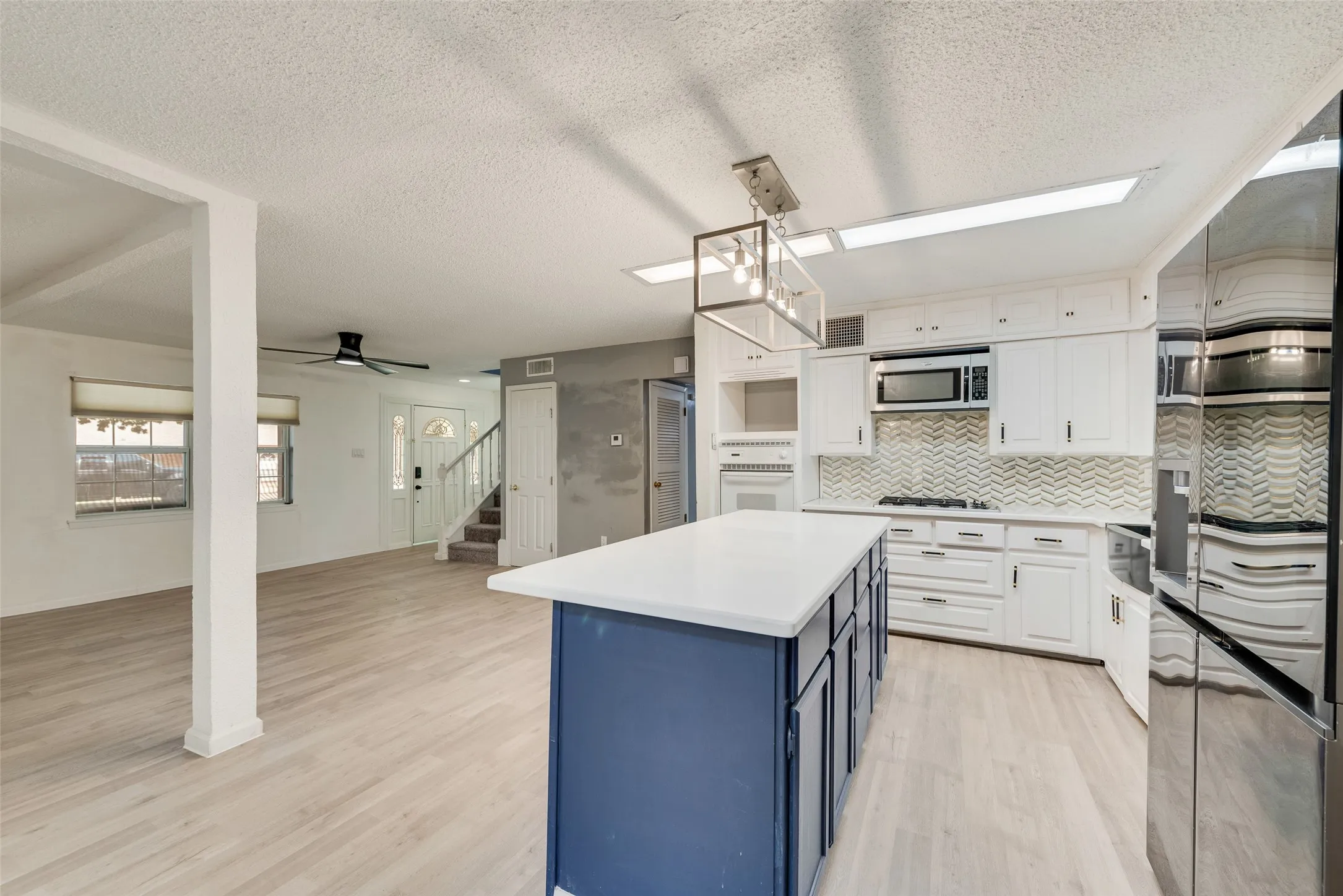 Kitchen featuring white cabinetry, chevron tile backsplash, stainless steel appliances, and a blue island with a white countertop