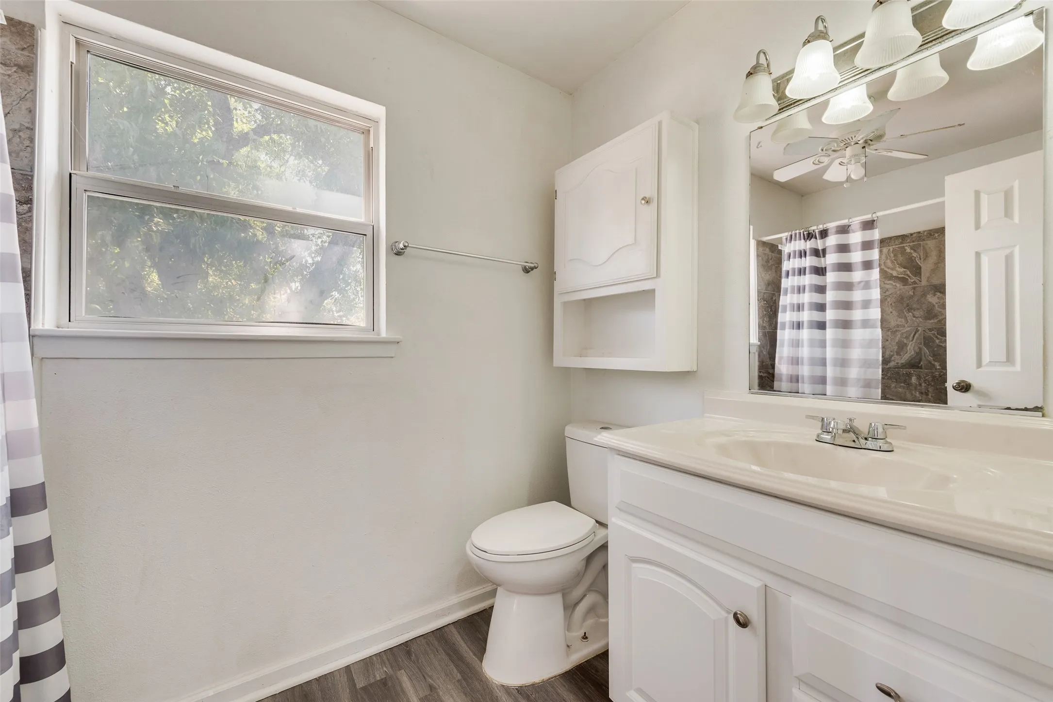 White vanity with integrated sink, wood-finish flooring, built-in wall cabinet, and overhead light fixture